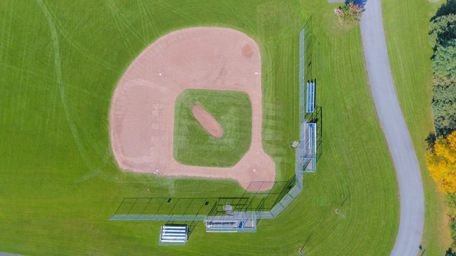 sports venues - Aerial shot of a baseball field with green grass in a park setting, empty and serene.
