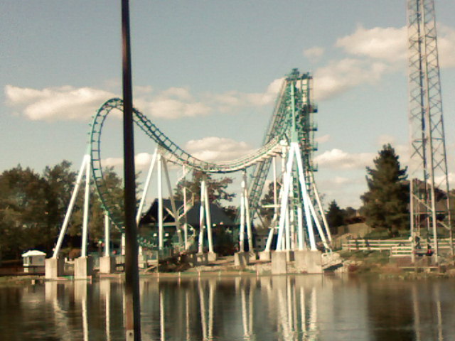 Boomerang roller coaster at Six Flags Darien Lake with teal track and white supports seen across the park lake