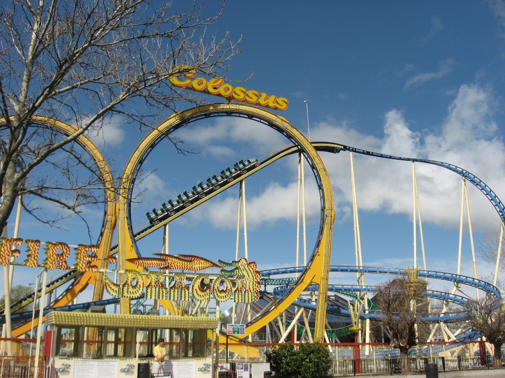 Colossus the Fire Dragon's marquee sign in front of the yellow double loops with a train cresting at Lagoon
