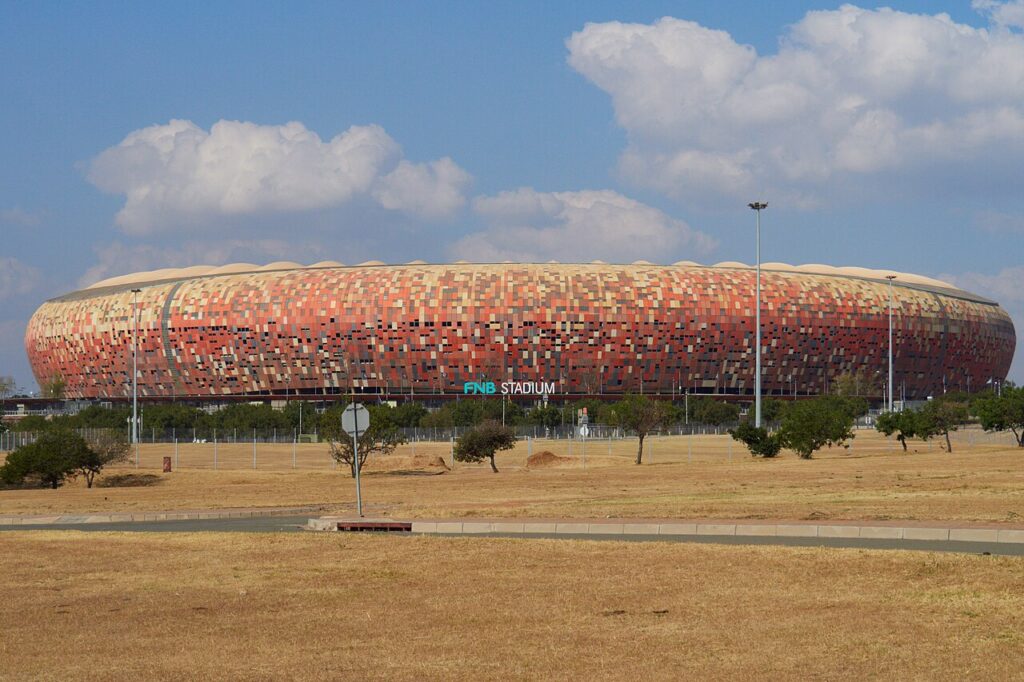 Exterior of FNB Stadium in Johannesburg, its calabash-shaped mosaic facade seen from the surrounding parklands