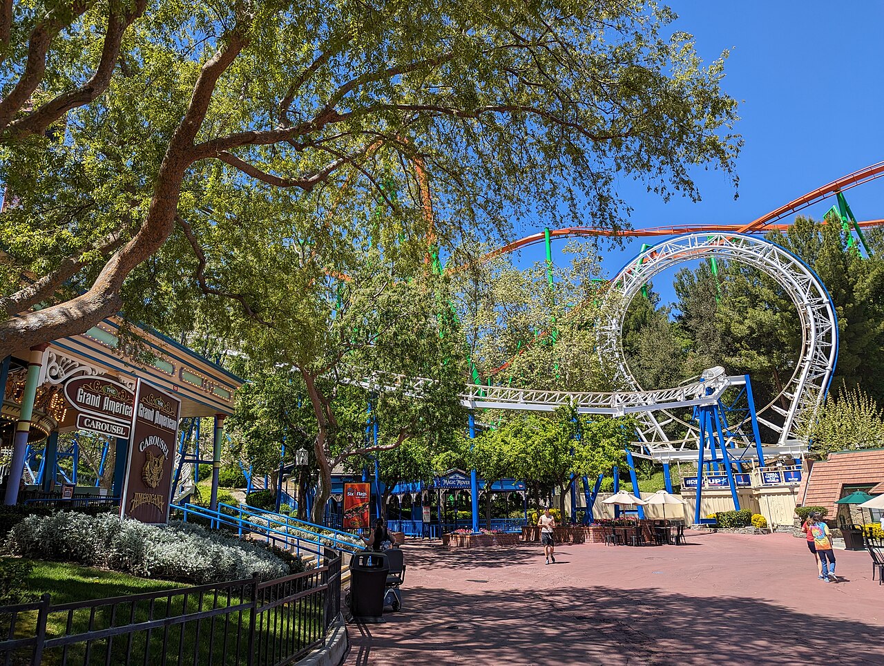 The Great American Revolution's white vertical loop rising above the trees, seen from the Grand America Carousel plaza