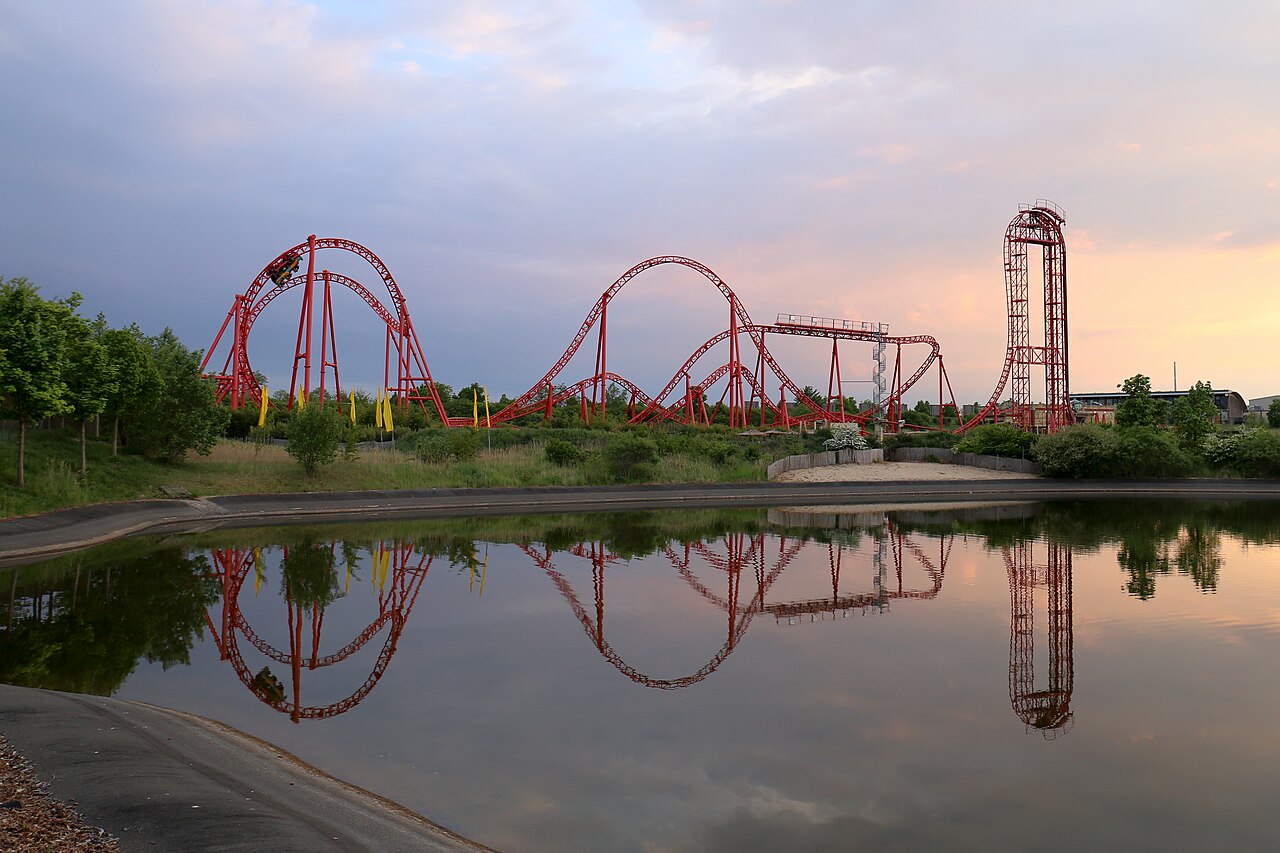 Huracan roller coaster's red track and vertical lift tower reflected in a lake at Belantis at dusk