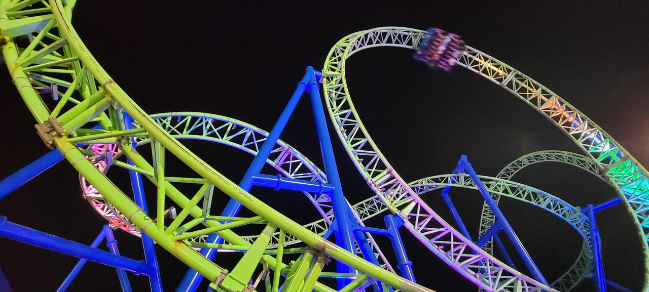 Hydrus roller coaster's green track and loop illuminated at night on Casino Pier with a train mid-course