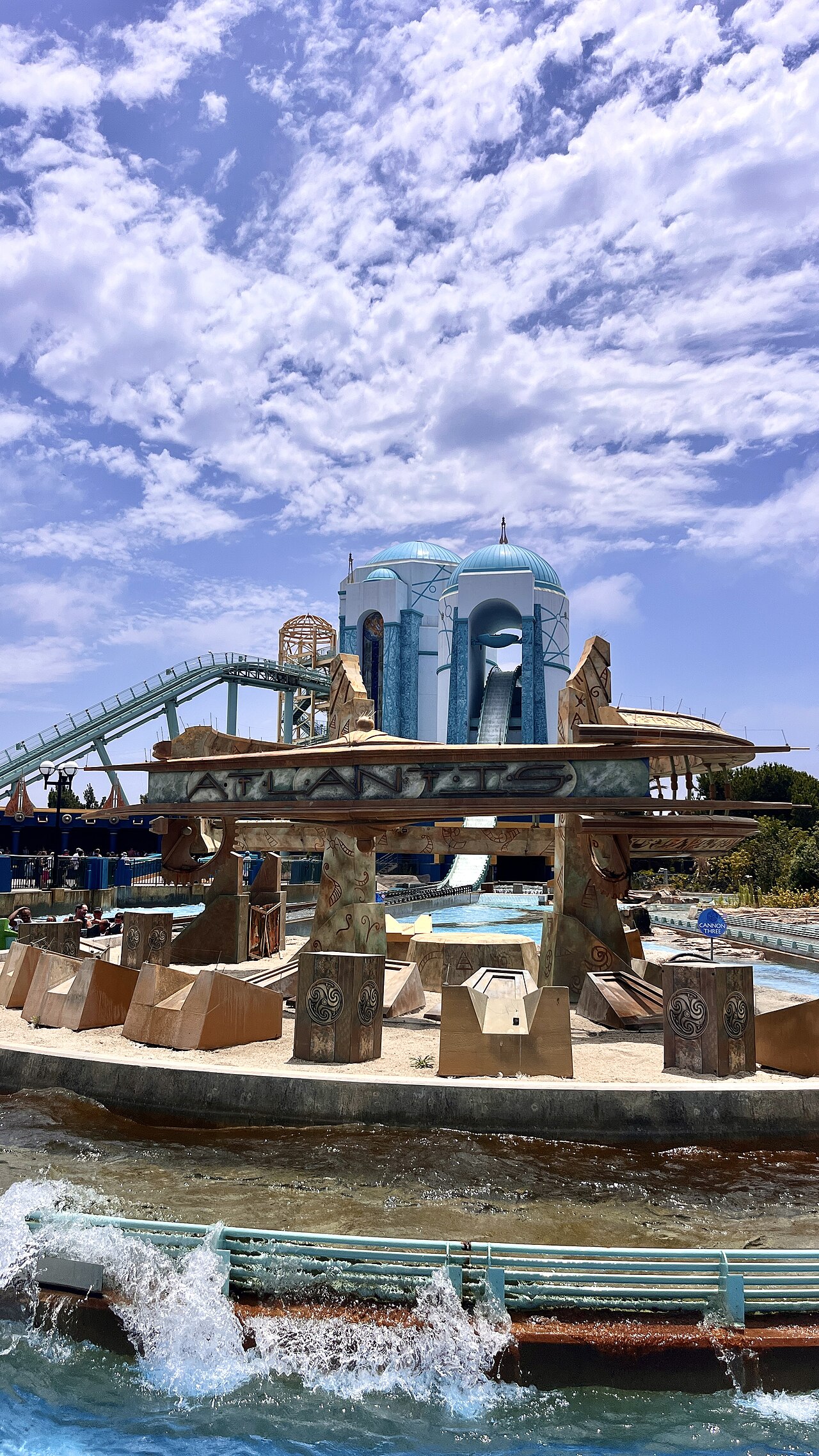 Atlantis sign in the foreground with Journey to Atlantis' domed towers and water slide behind at SeaWorld San Diego