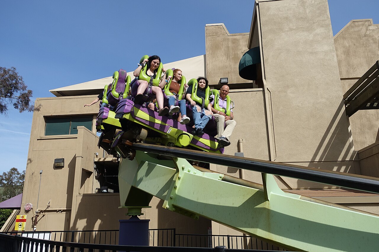 A green and purple Medusa floorless train leaves the station with riders' feet dangling