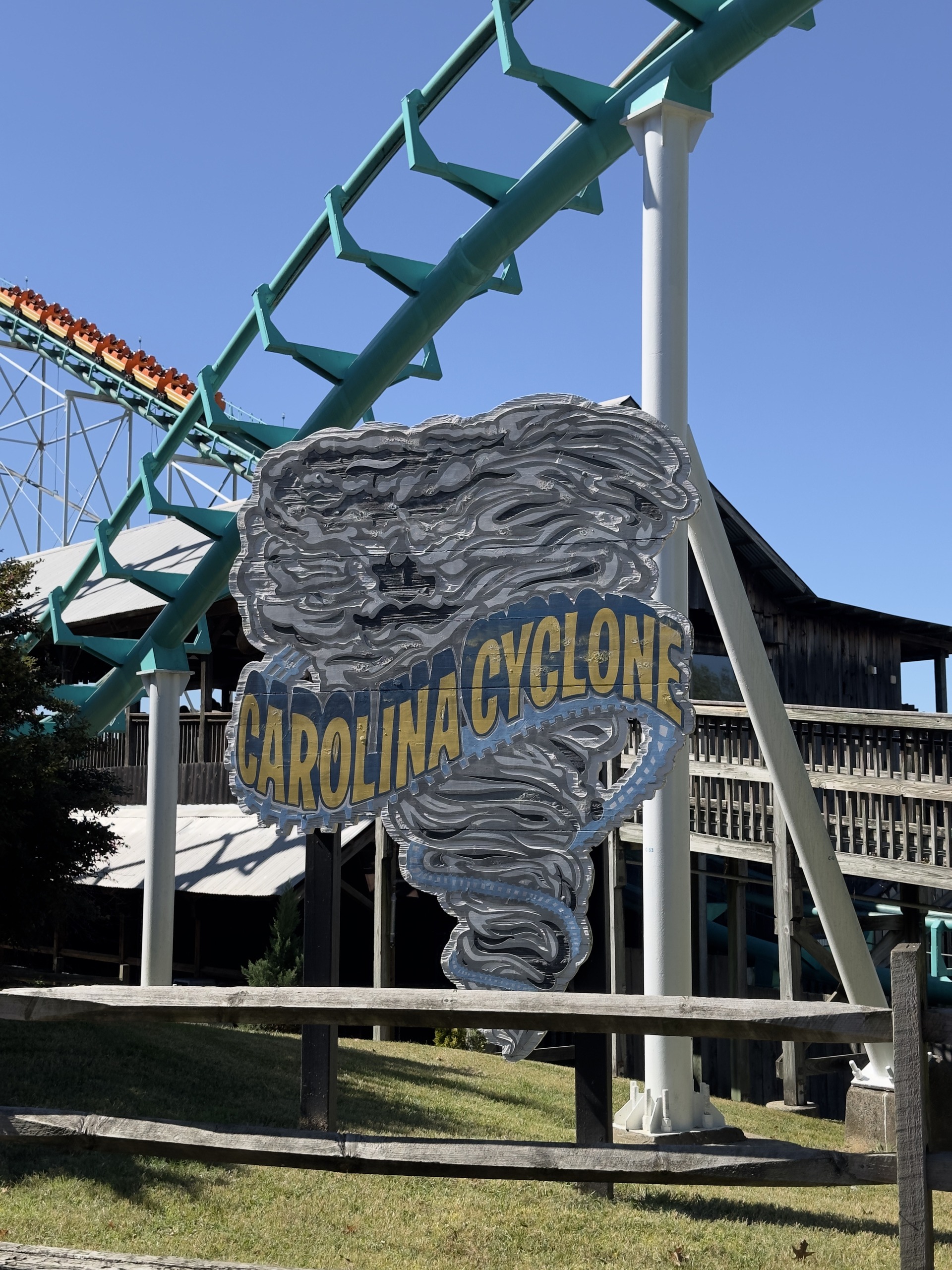 The Carolina Cyclone sign beside the teal track with an orange train on the lift behind it, Carowinds, October 2024