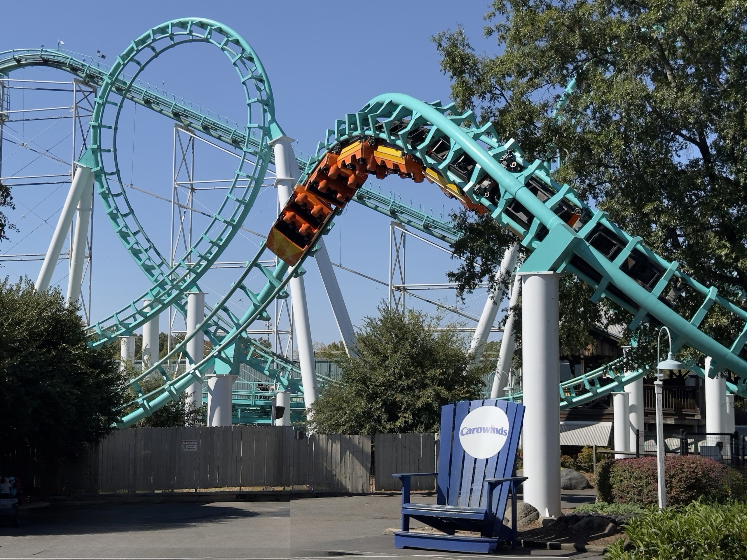 An orange Carolina Cyclone train in the corkscrew above the giant blue Carowinds chair, October 2024