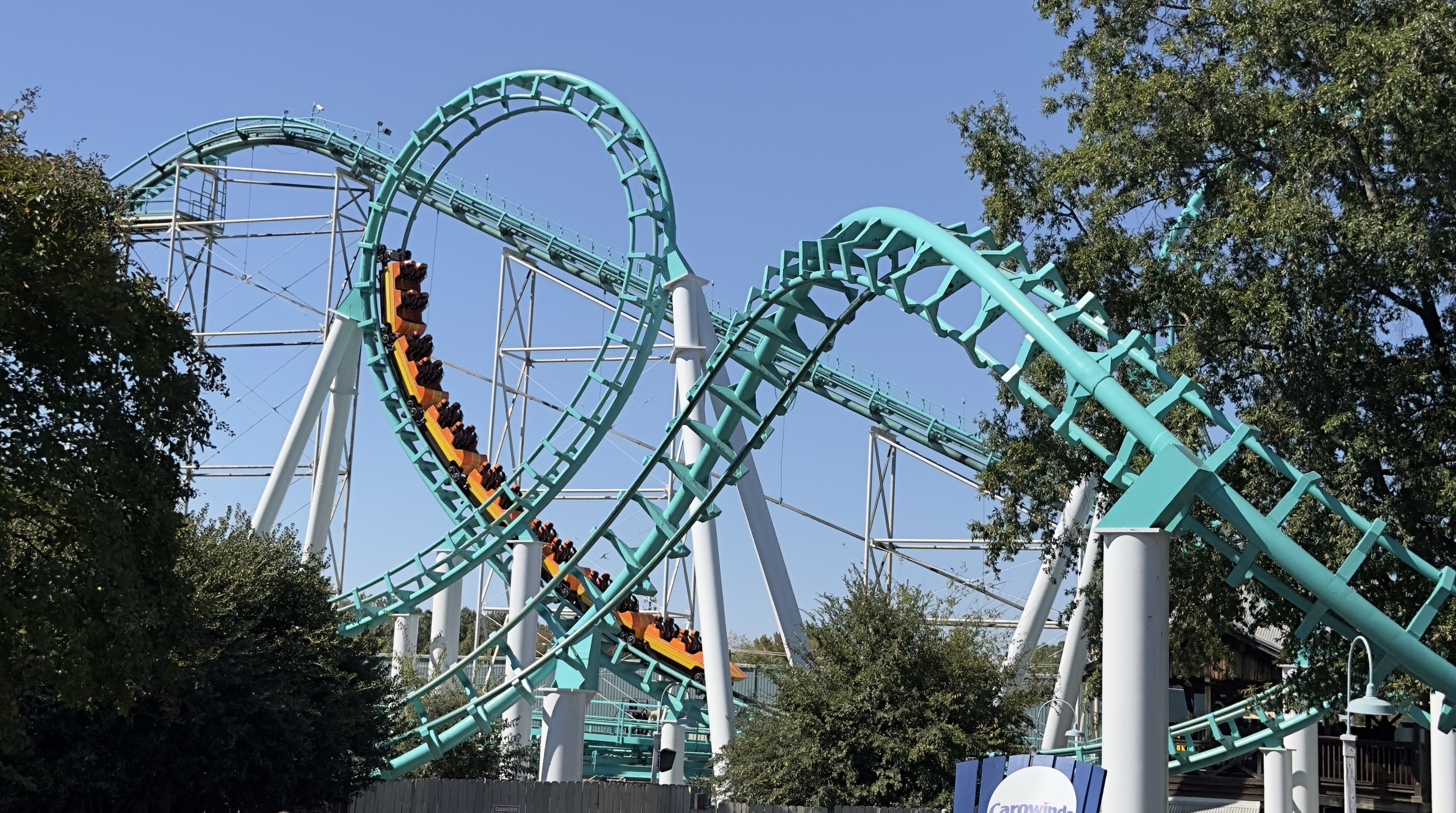 An orange Carolina Cyclone train diving through the teal double corkscrew, Carowinds, October 2024