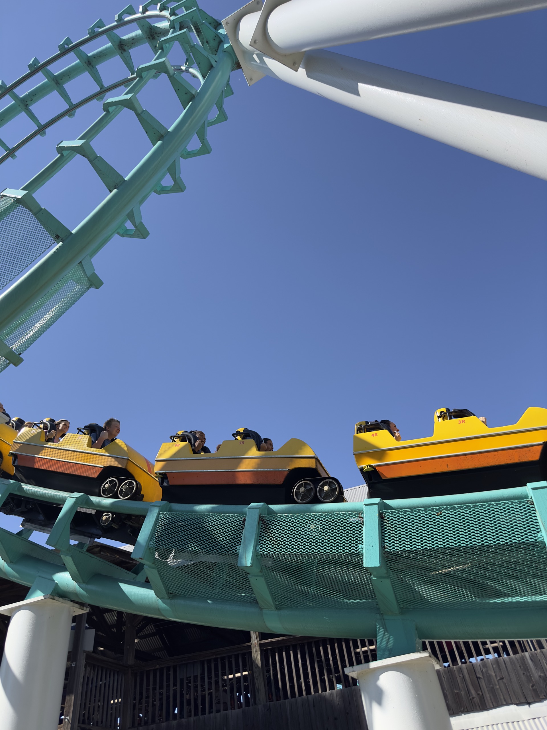 A yellow Carolina Cyclone train rounding a banked curve below a white support, Carowinds, October 2024