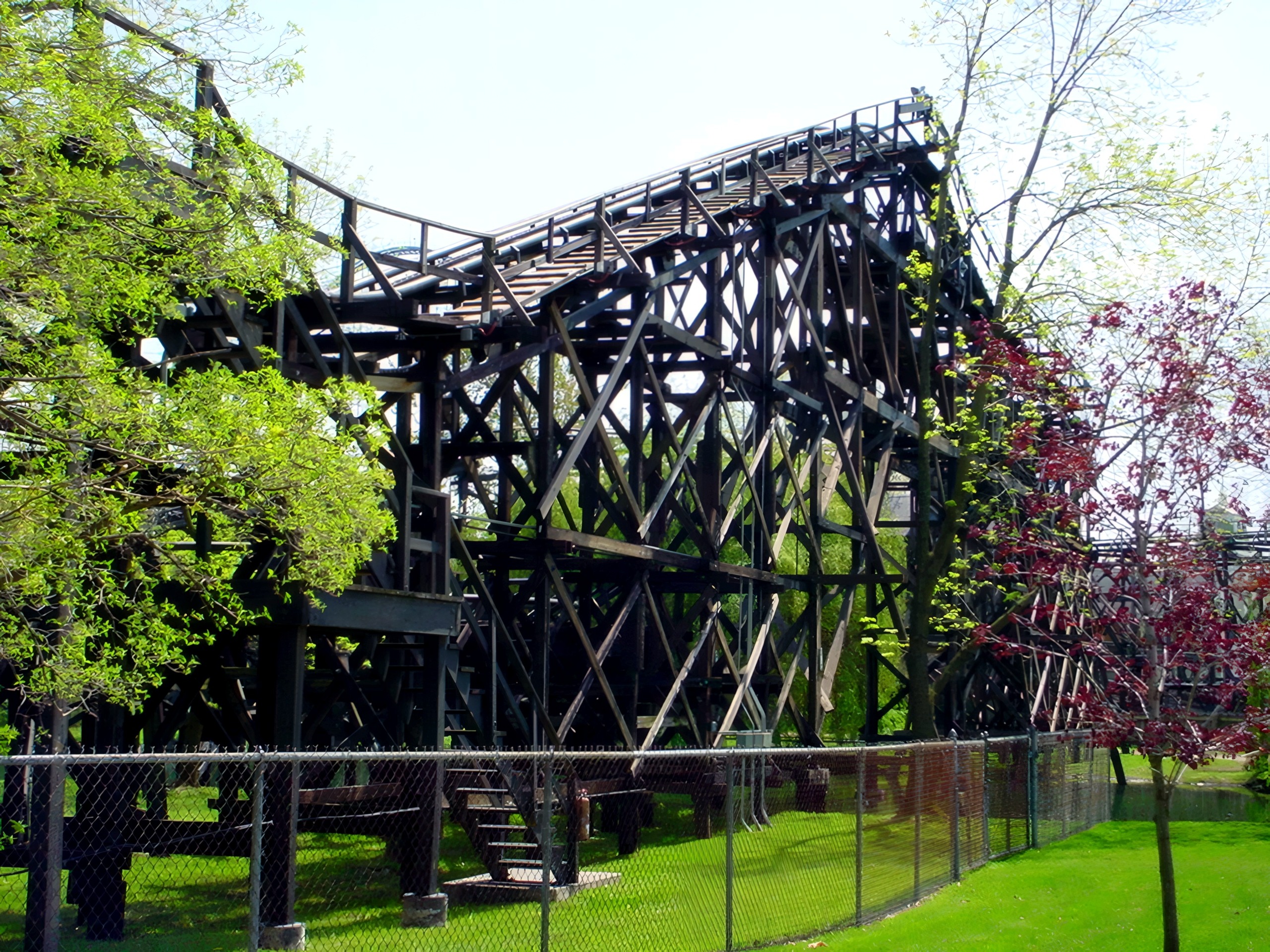 Dark wooden coaster structure framed by trees and fence, Cedar Creek Mine Ride