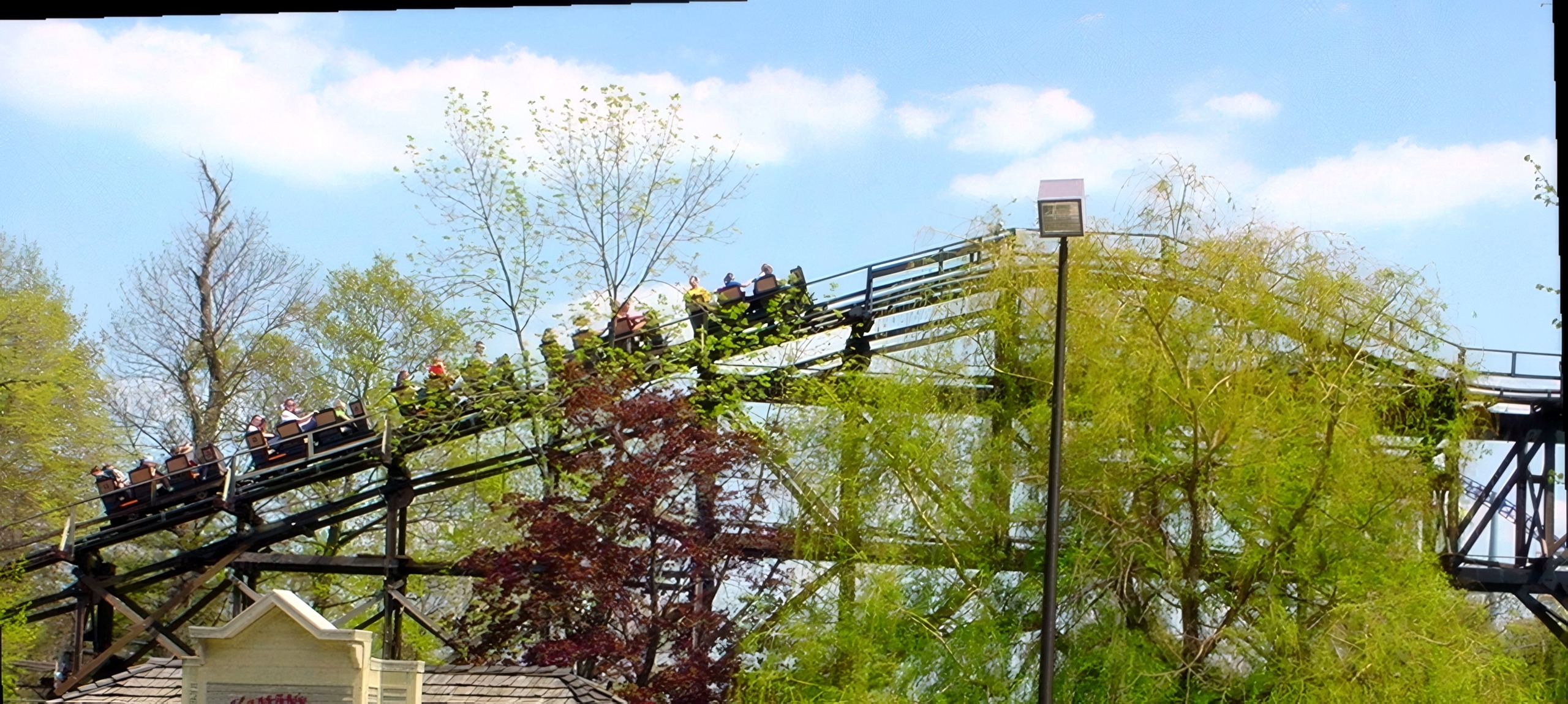 Distant coaster train on wooded trestle, guests walking path, Cedar Creek Mine Ride