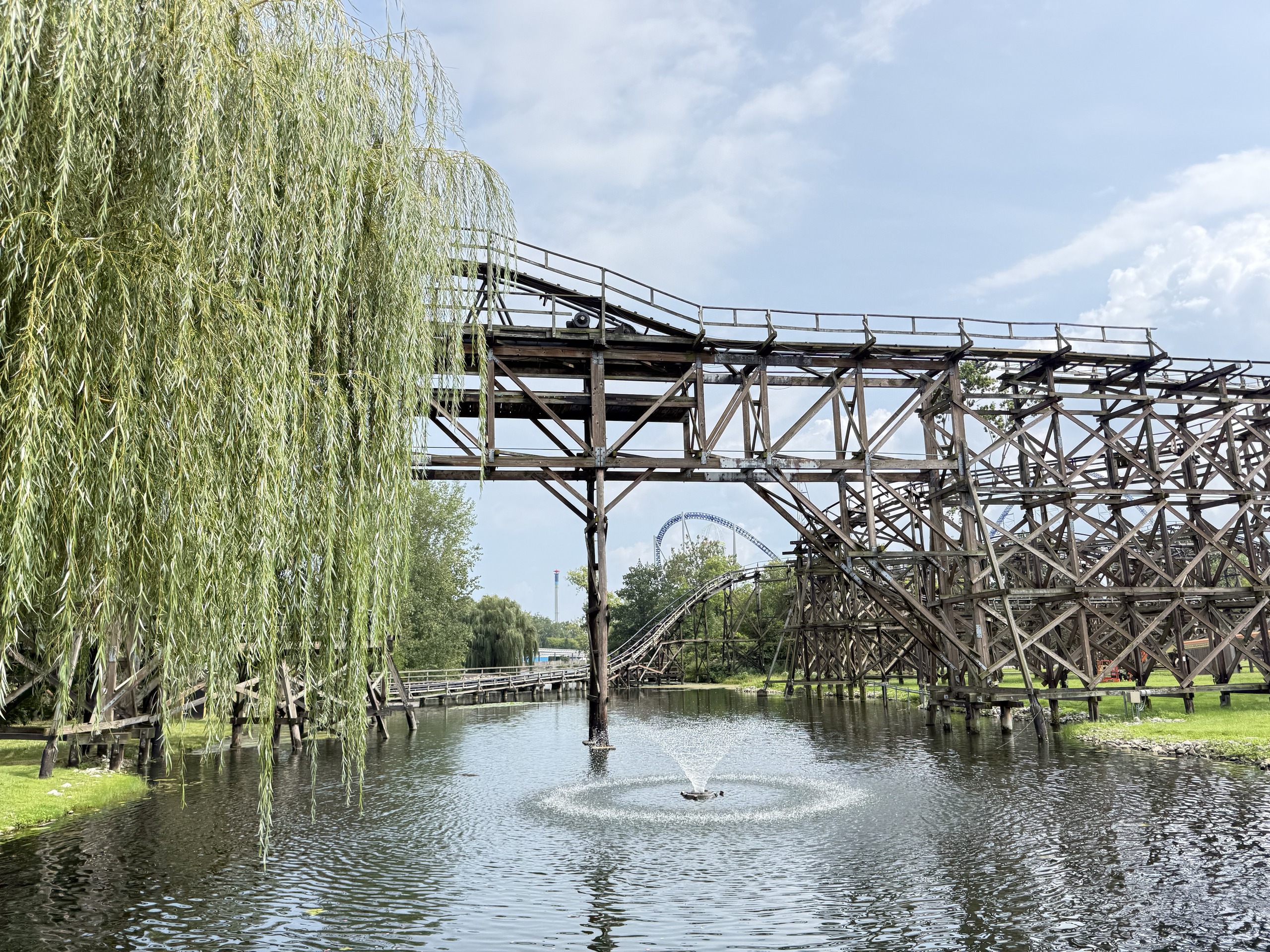 Cedar Creek Mine Ride's wooden trestle over the lagoon and fountain with a willow in the foreground