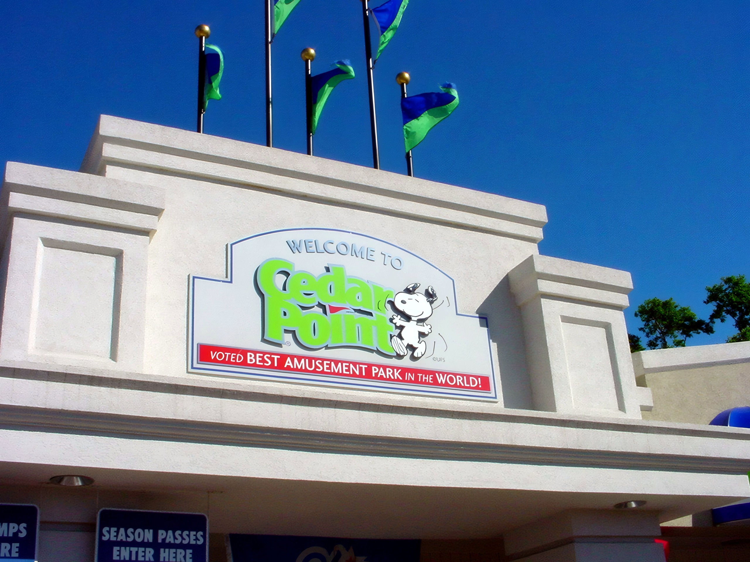 The Welcome to Cedar Point main entrance sign with flags against a blue sky at Cedar Point, July 2003