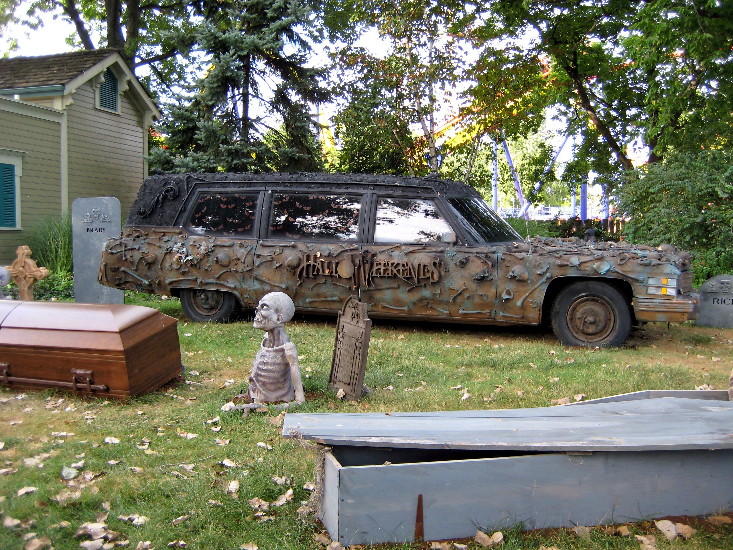 The HalloWeekends hearse and graveyard props with coaster track behind the trees at Cedar Point, September 2007
