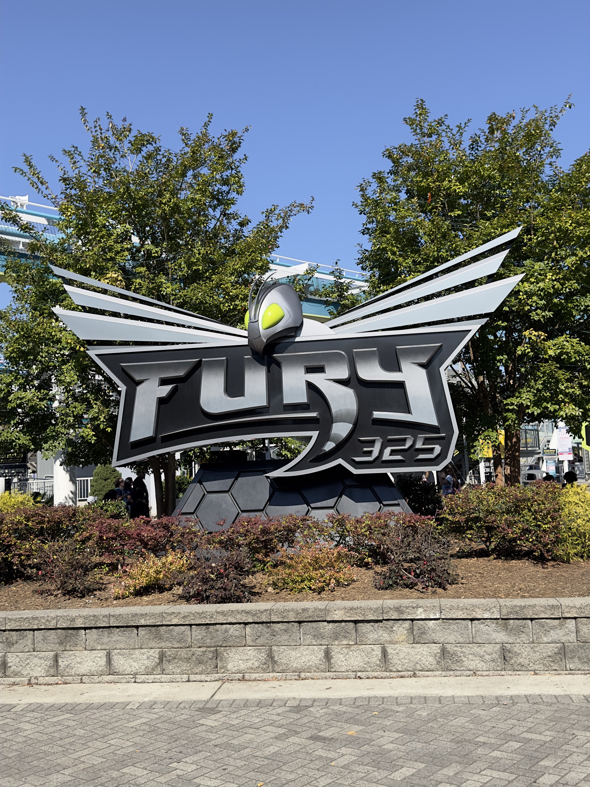The winged Fury 325 entrance sign above a planter on the Carowinds midway, October 2024