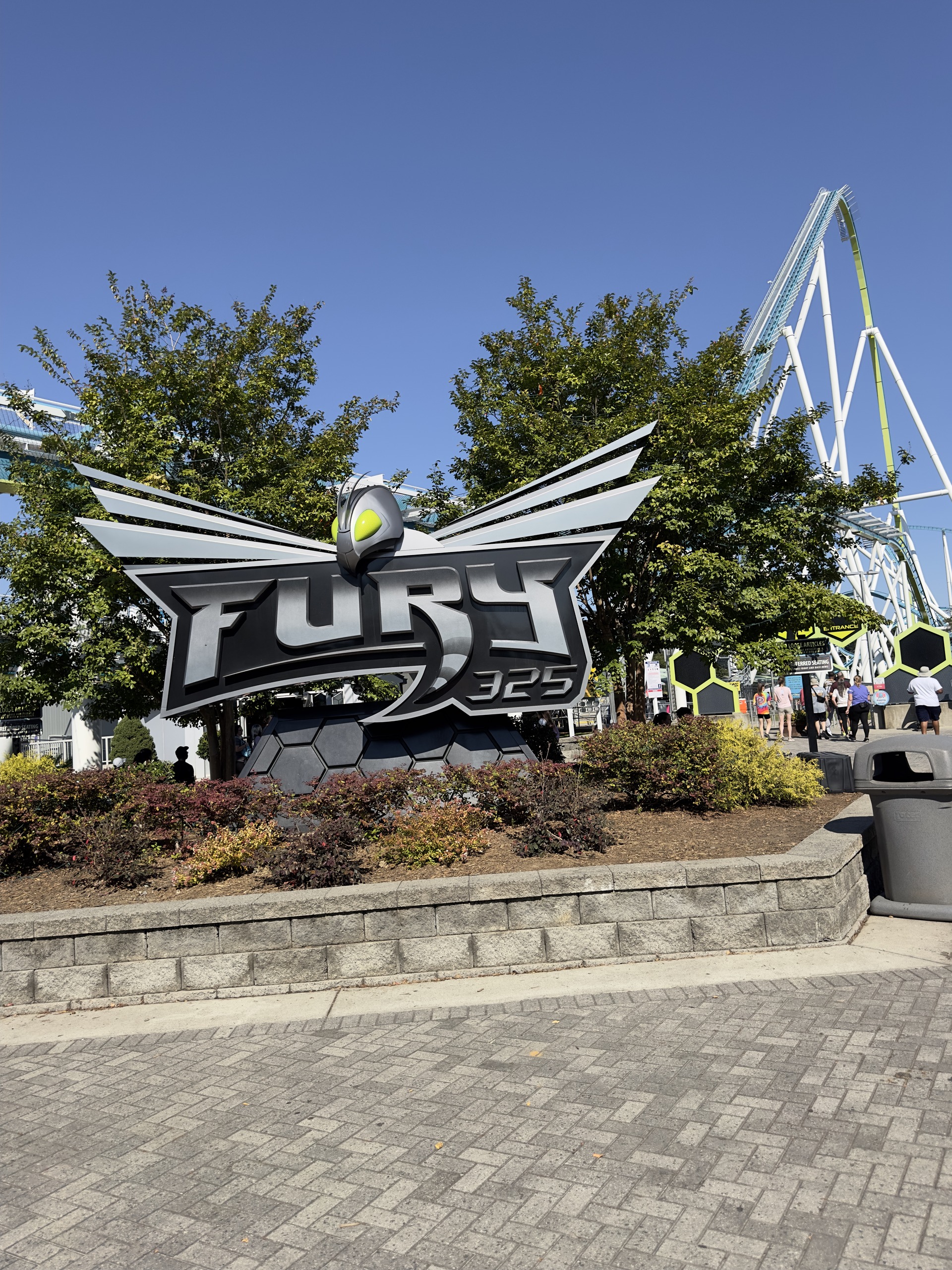 The Fury 325 winged sign in its planter with the lift behind the trees, Carowinds, October 2024