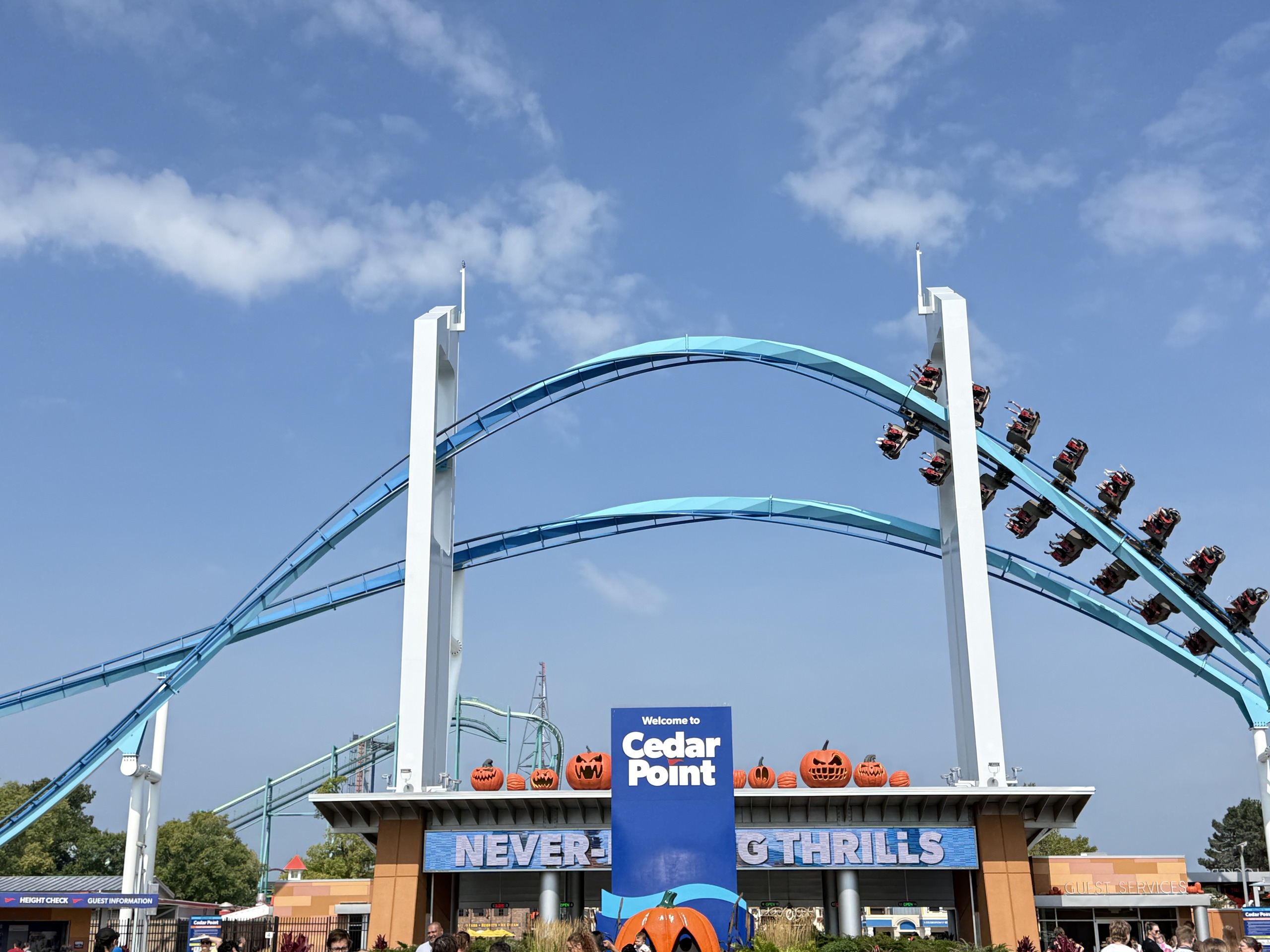 A GateKeeper wing coaster train flying through the keyhole tower above the Cedar Point entrance sign lined with pumpkins