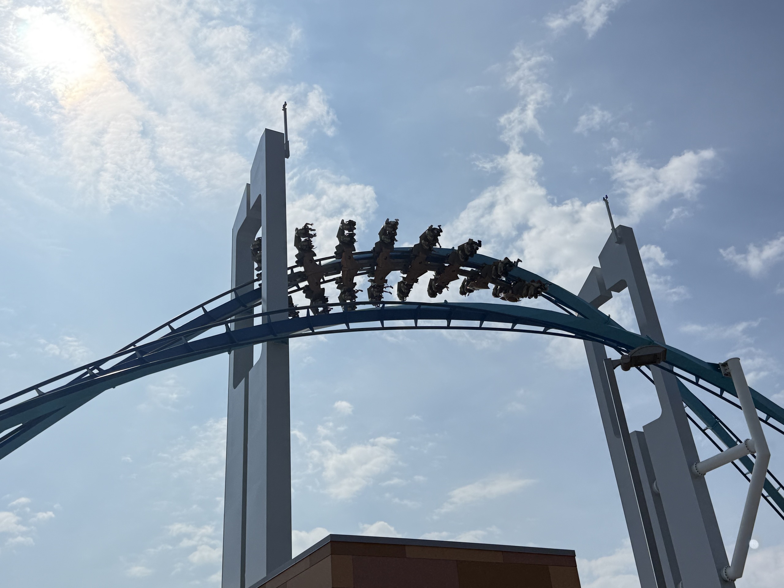 A GateKeeper wing train inverting through a keyhole tower, teal track against a cloudy sky