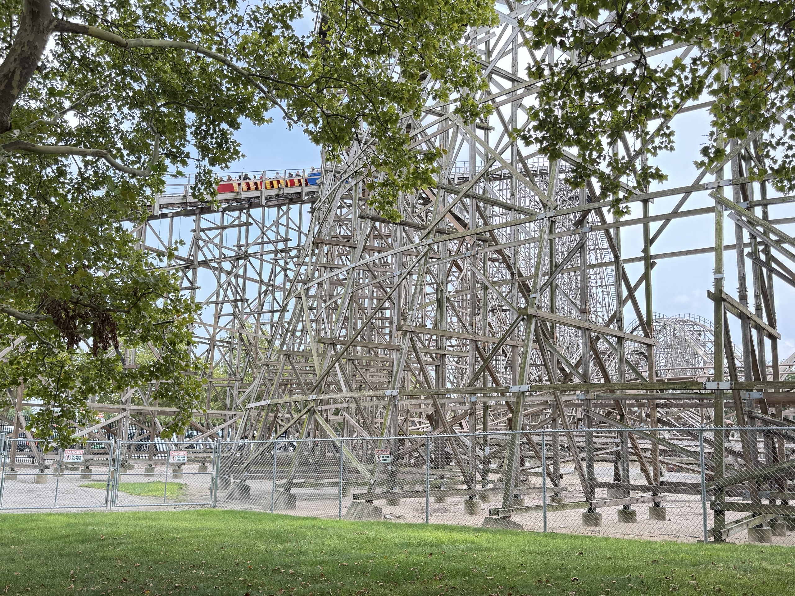 A Gemini train cresting the lift hill, framed by trees and the wooden structure