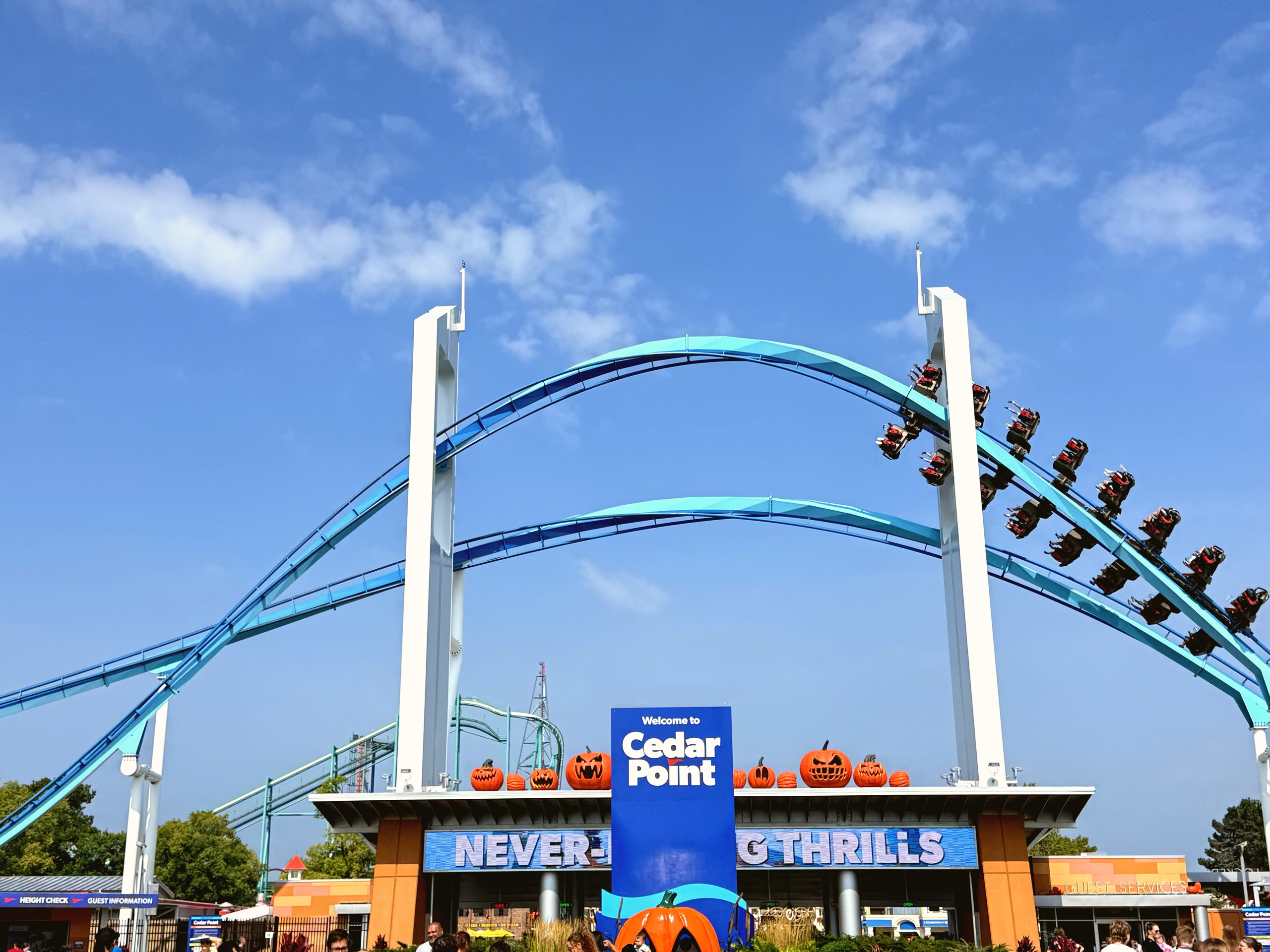 GateKeeper wing coaster train flying over the Cedar Point entrance sign lined with jack-o-lanterns