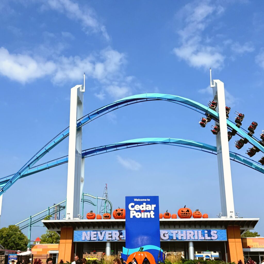 GateKeeper wing coaster train flying over the Cedar Point entrance sign lined with jack-o-lanterns