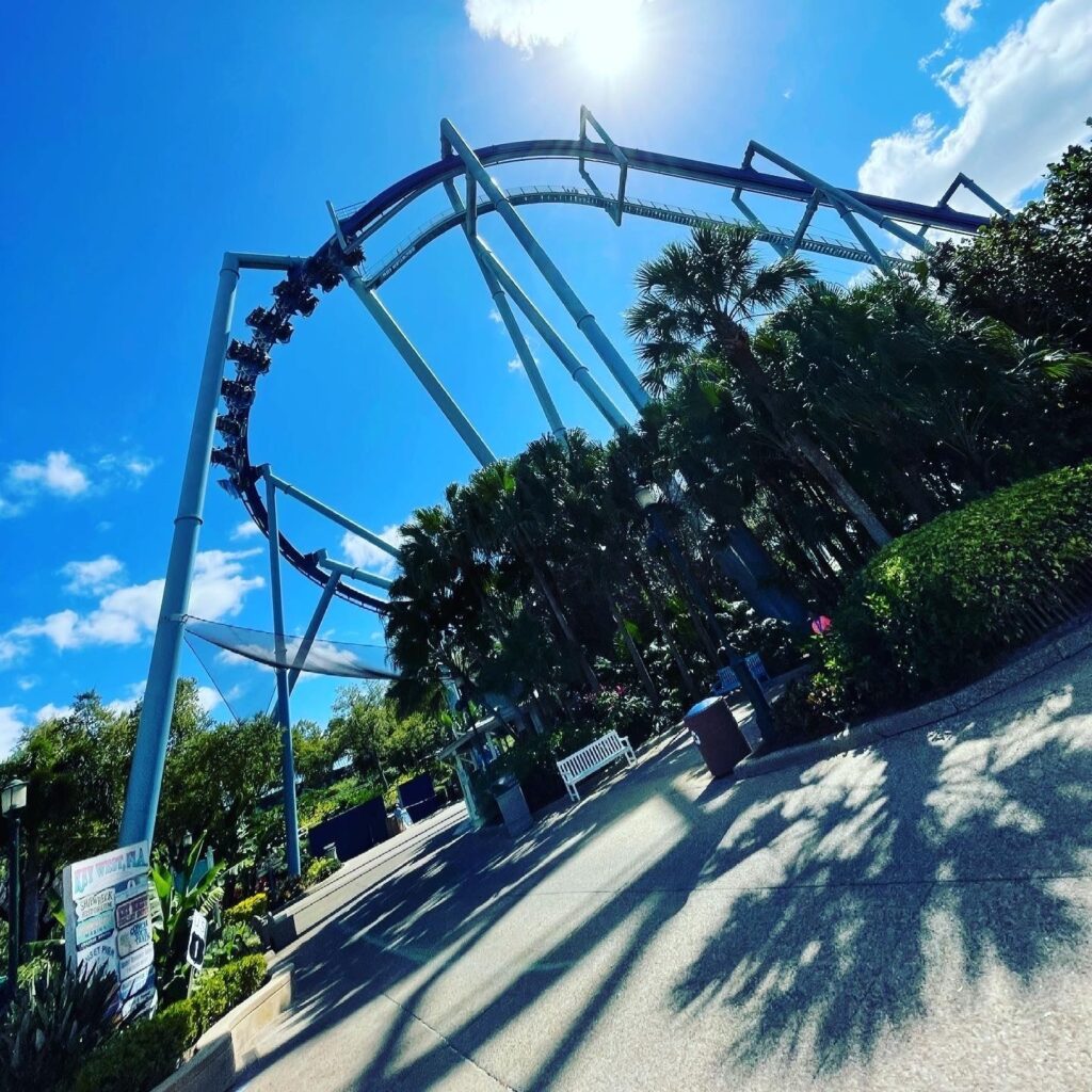 Manta's dark blue track and light blue supports arcing over the midway with a train at the top of the inversion, SeaWorld Orlando, March 2021