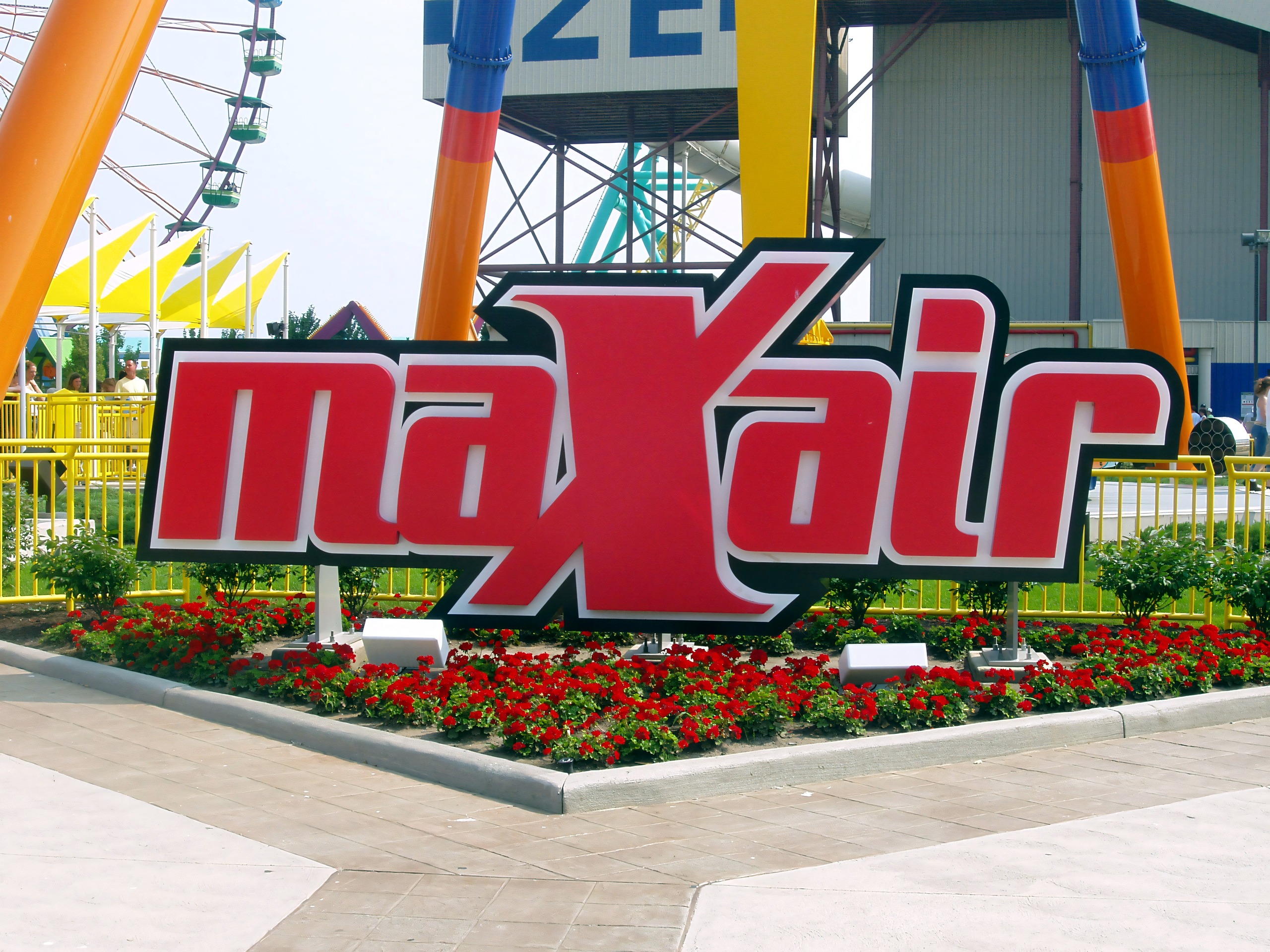 The maXair sign among red flowers, with the ride's tower legs and a Ferris wheel behind, at Cedar Point, July 2005