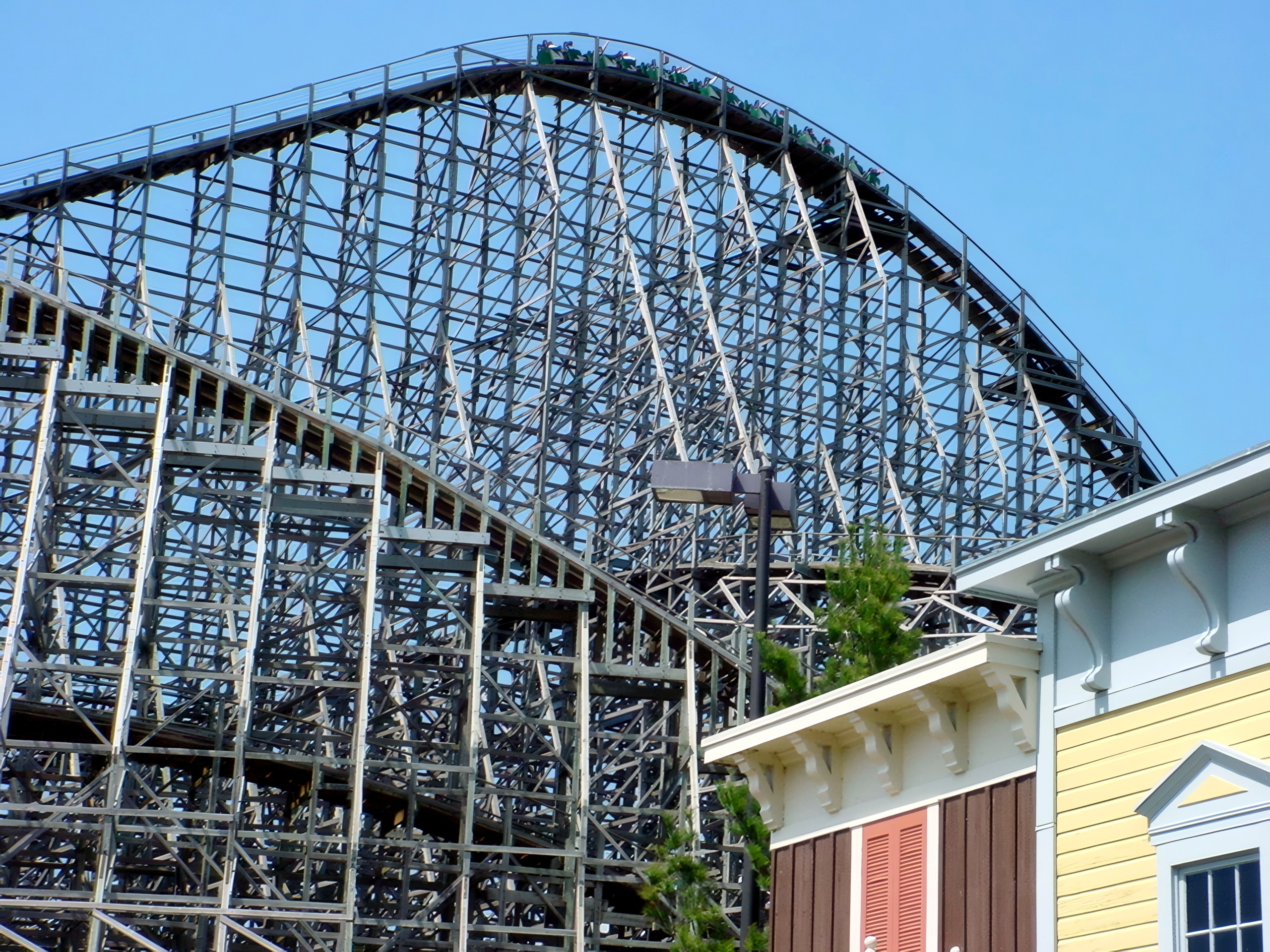 Wooden coaster train cresting hill above yellow building, May 5, 2002.
