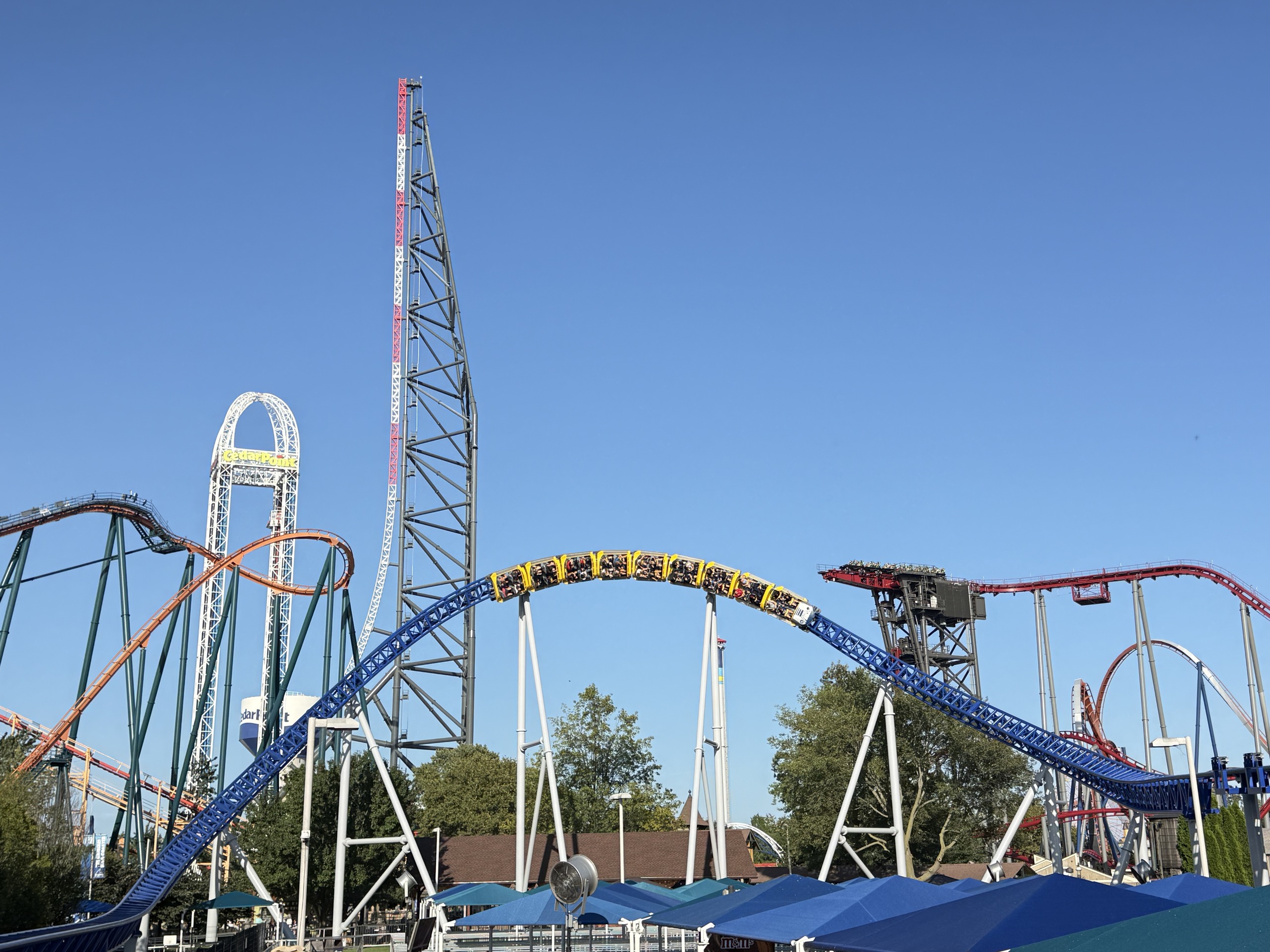 A Millennium Force train cresting the blue overbanked turn with the Top Thrill 2 tower behind