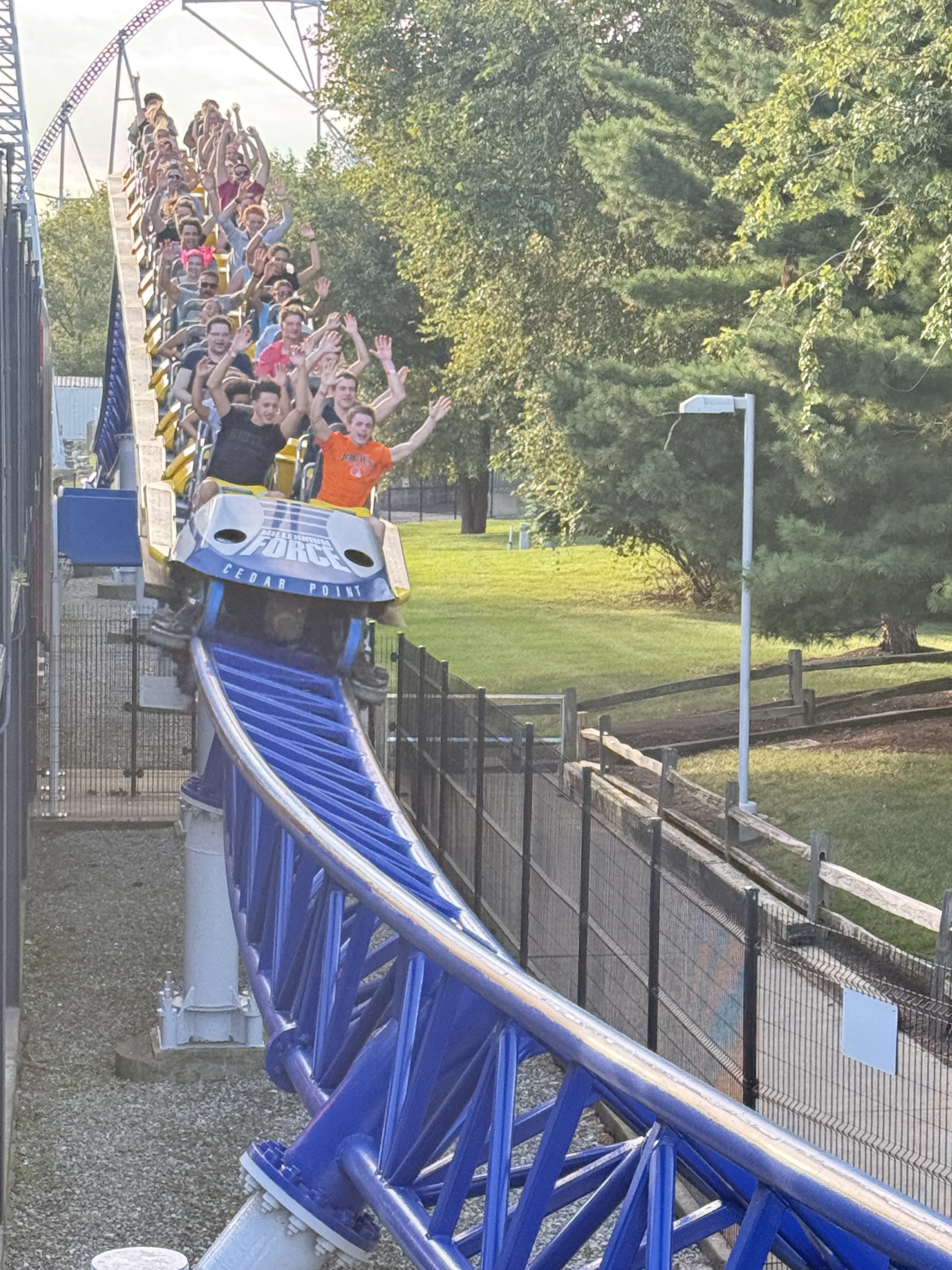 A close-up of a Millennium Force train with riders waving and the Cedar Point logo on the front car