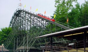 A red Phoenix train climbing the flag-lined lift hill above the station at Knoebels, July 2003