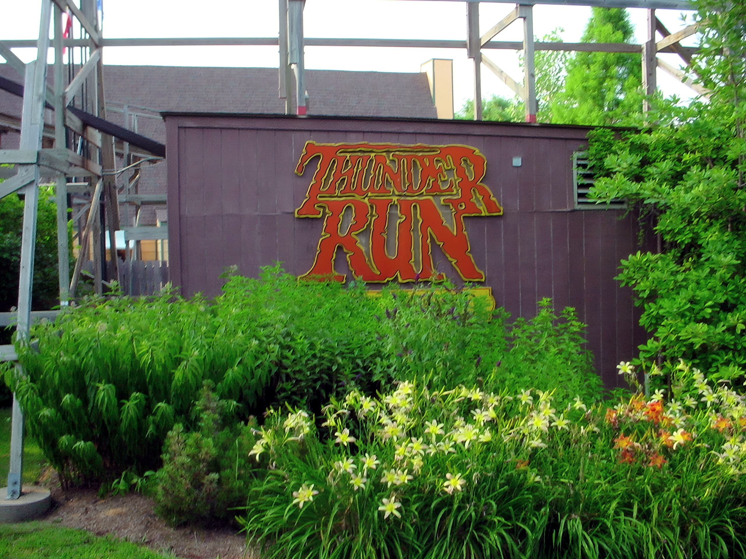 The Thunder Run sign on a building beside the wooden structure, framed by daylilies at Six Flags Kentucky Kingdom, July 2002