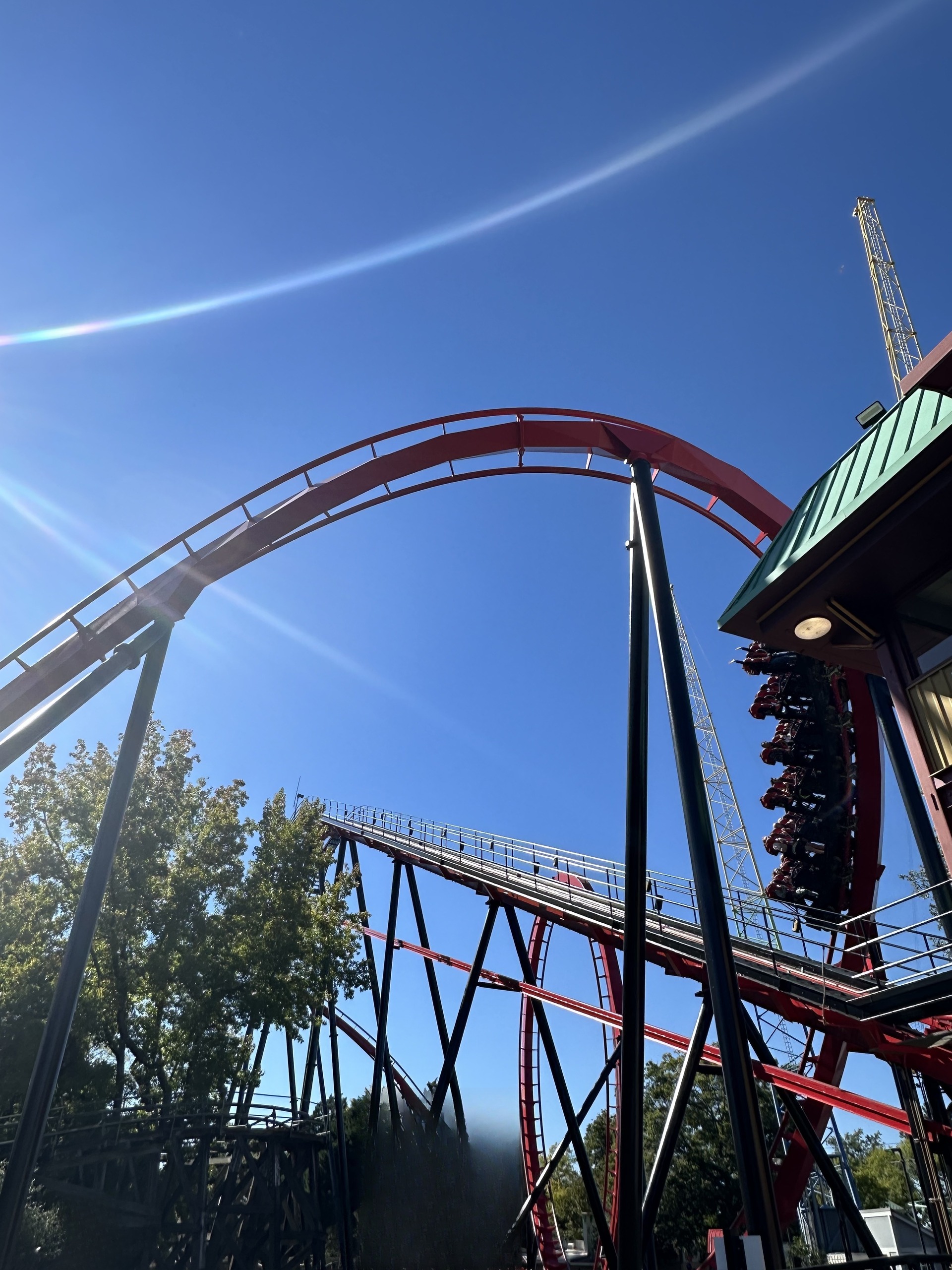 A Vortex train dropping past the station roof beside the loop, Carowinds, October 2024