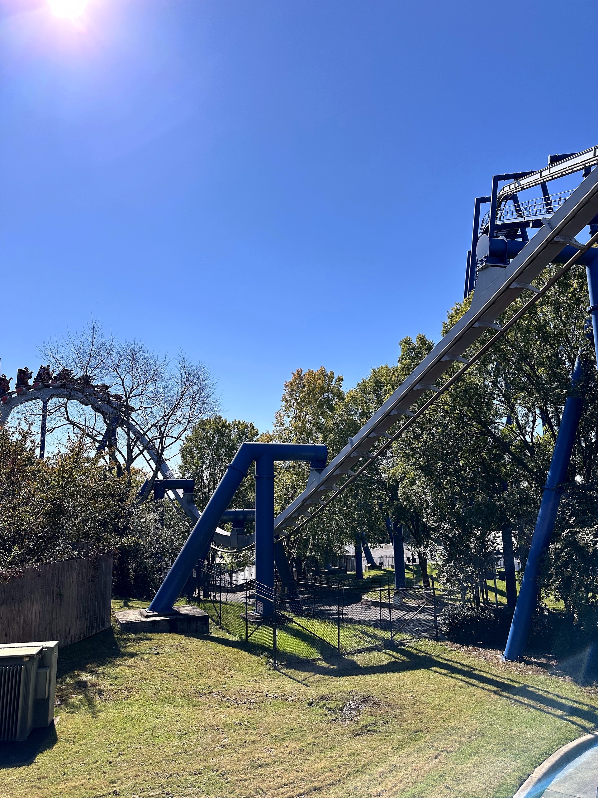 Afterburn's gray inverted track and blue supports stretching across a grassy lawn at Carowinds, October 2024