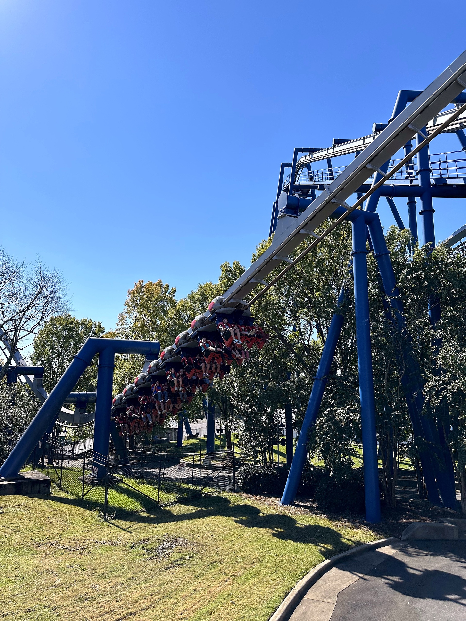 An Afterburn train with riders' legs dangling as it sweeps down the track above the lawn at Carowinds, October 2024