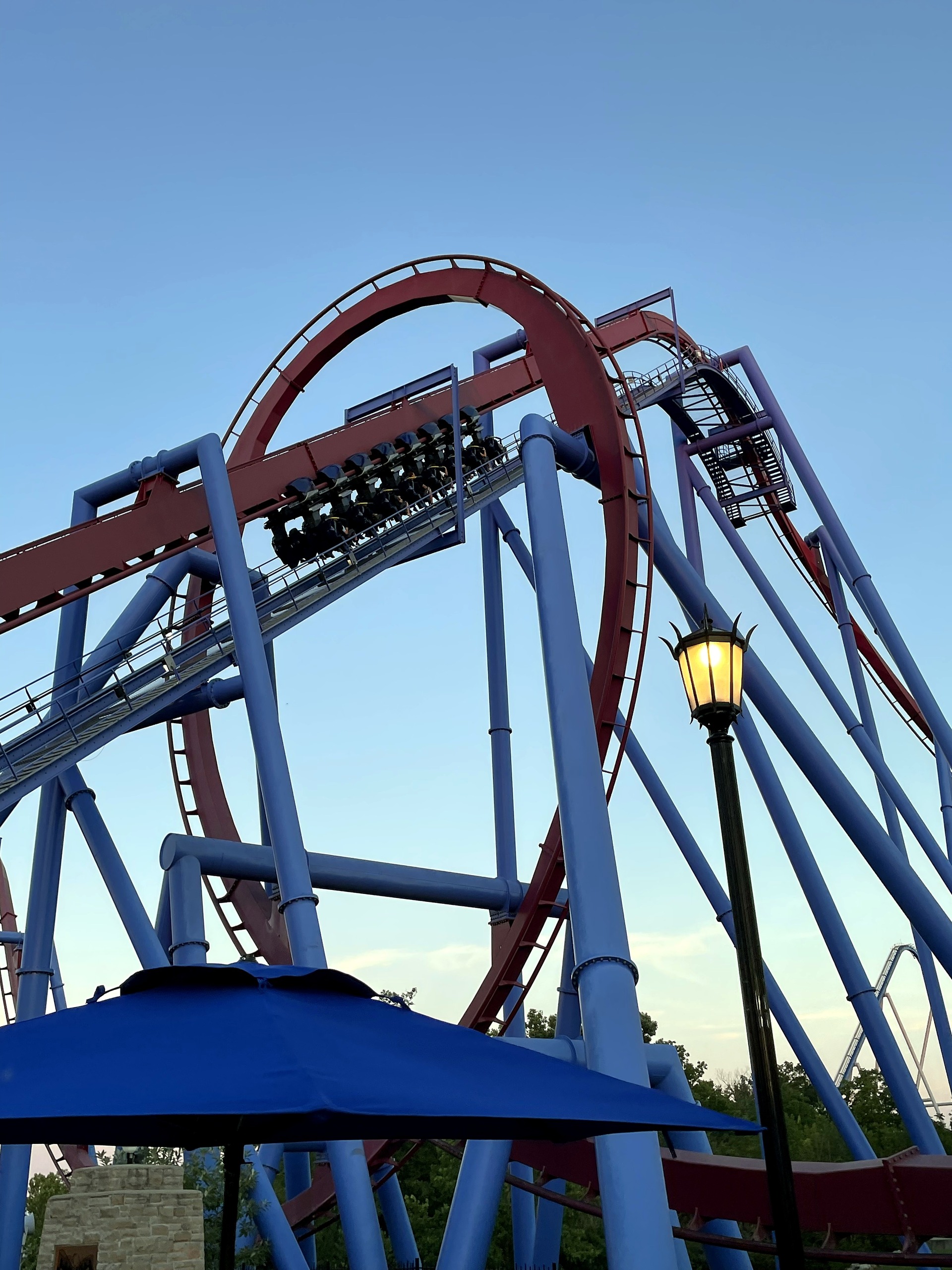 A Banshee train on the lift and the loop above a blue patio umbrella, Kings Island, July 2022
