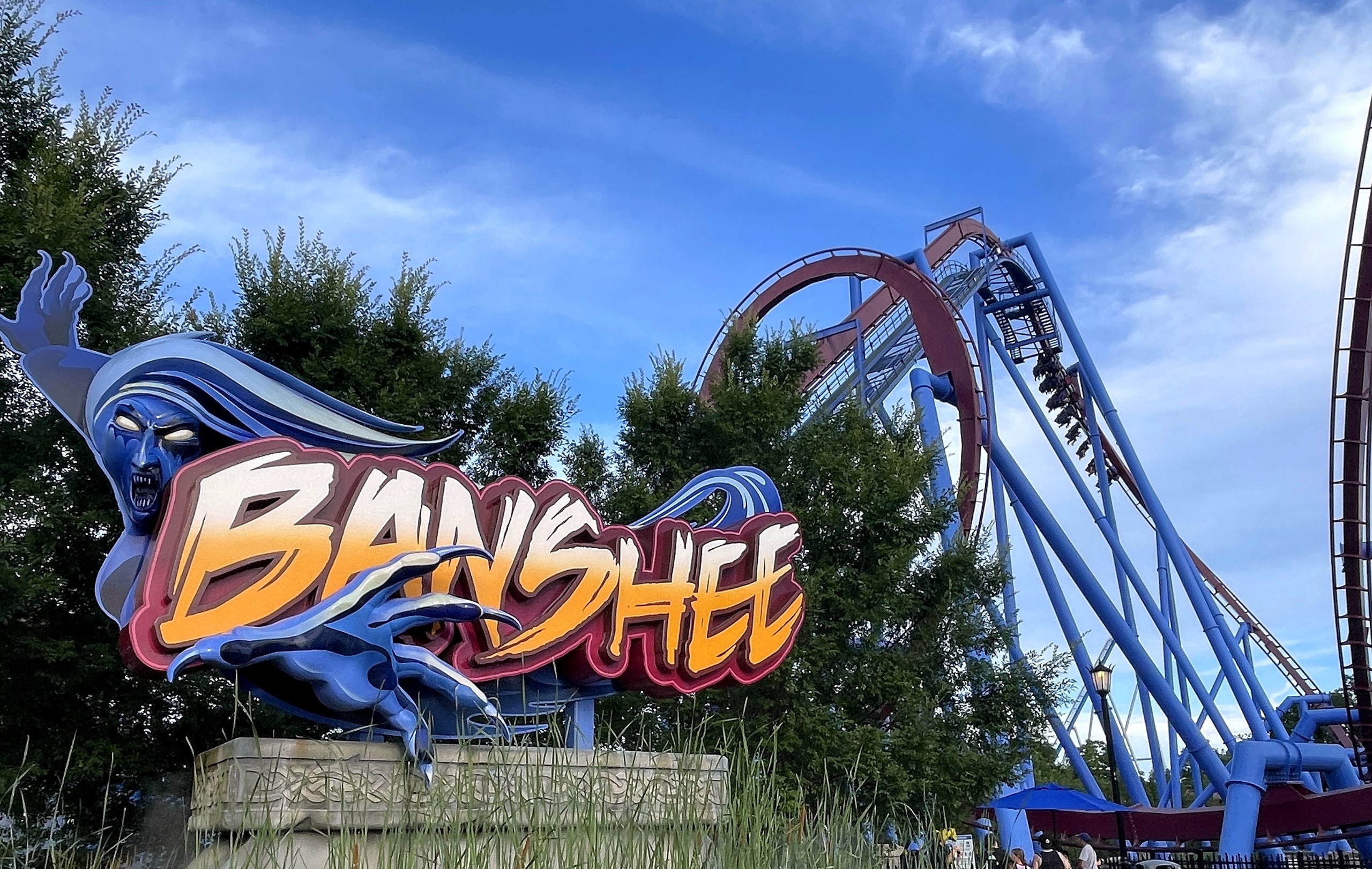The Banshee sign with the lift hill and loop rising behind the trees, Kings Island, July 2022