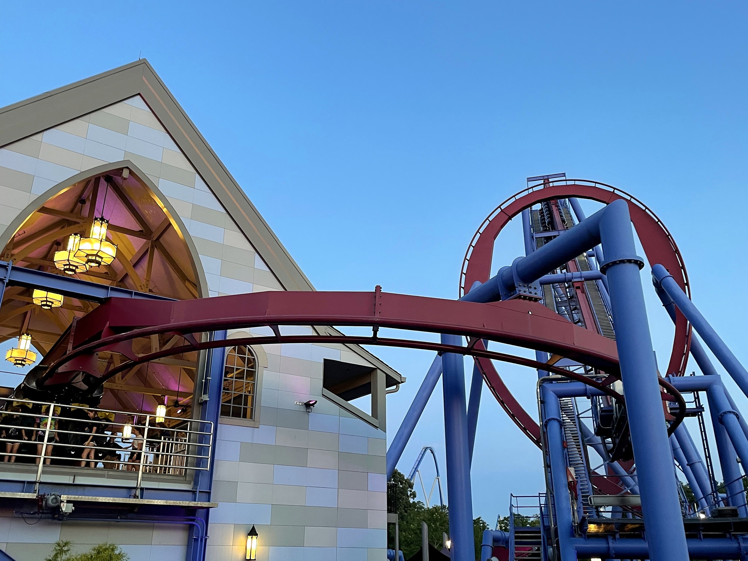 Banshee's track and loop beside the gabled building with its chandeliers glowing, Kings Island, July 2022