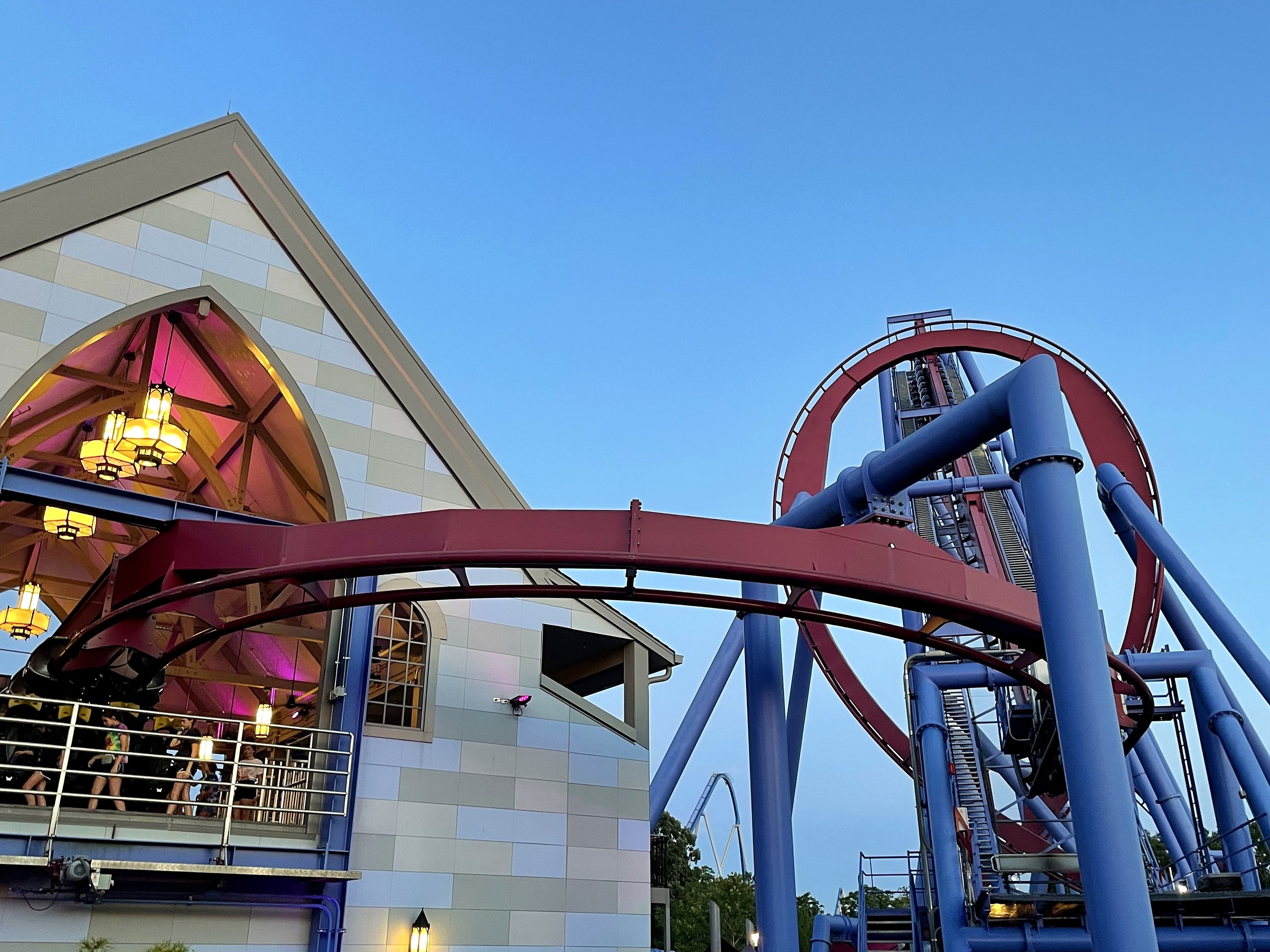 Banshee's maroon track curving past a gabled building lit by chandeliers, the loop beyond, Kings Island, July 2022