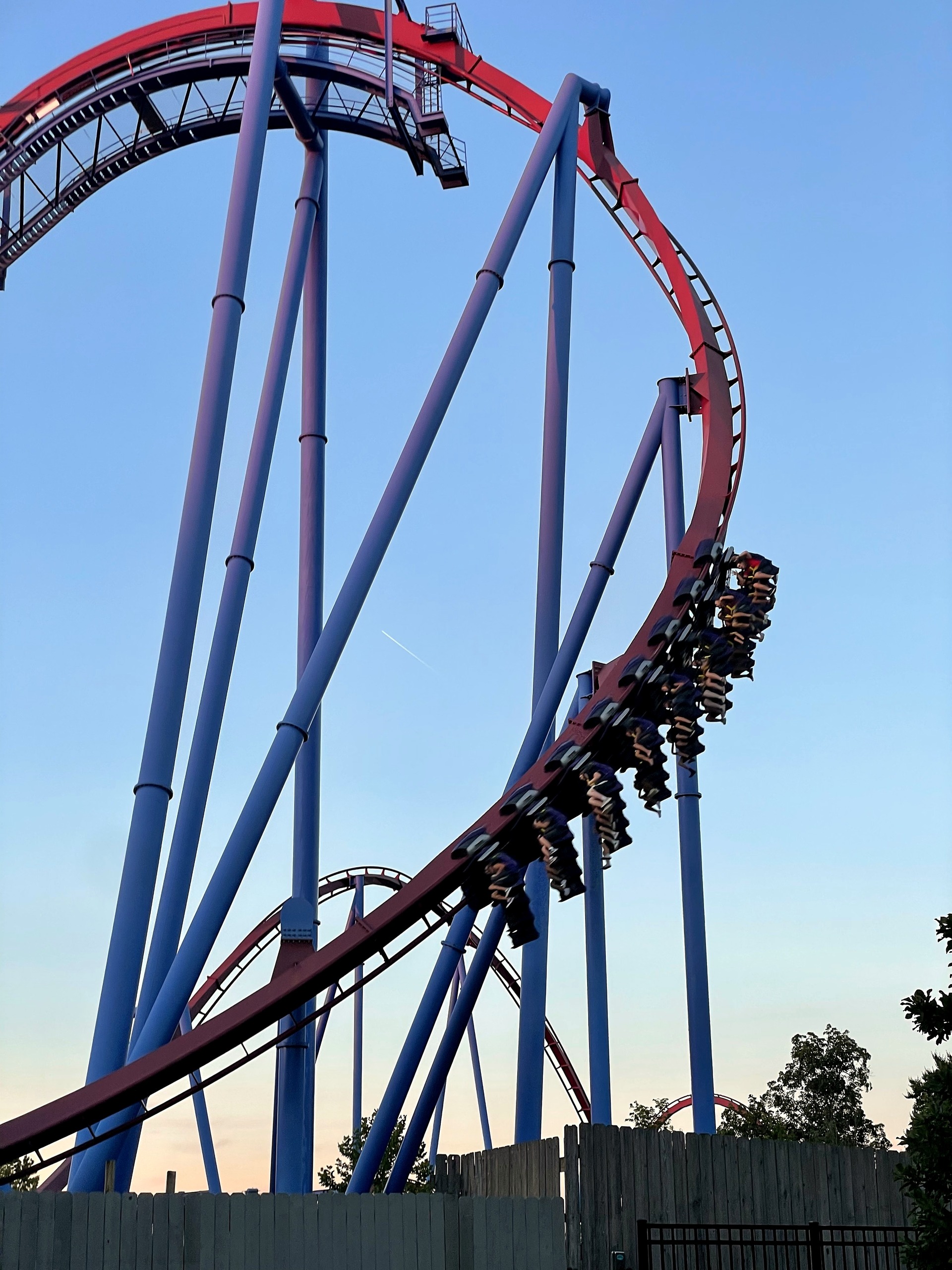 A Banshee train swinging down the maroon curve between the blue supports, Kings Island, July 2022