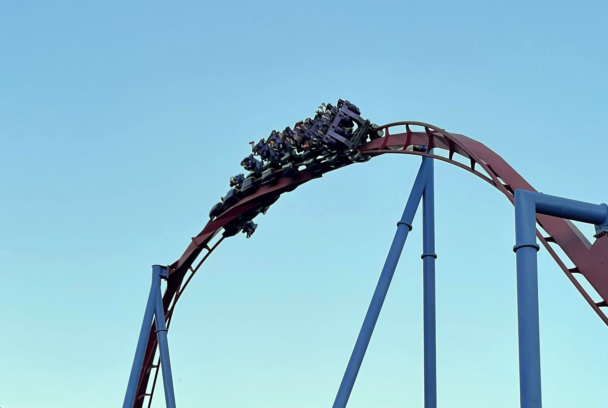 A Banshee train upside down at the top of an inversion against a pale sky, Kings Island, July 2022