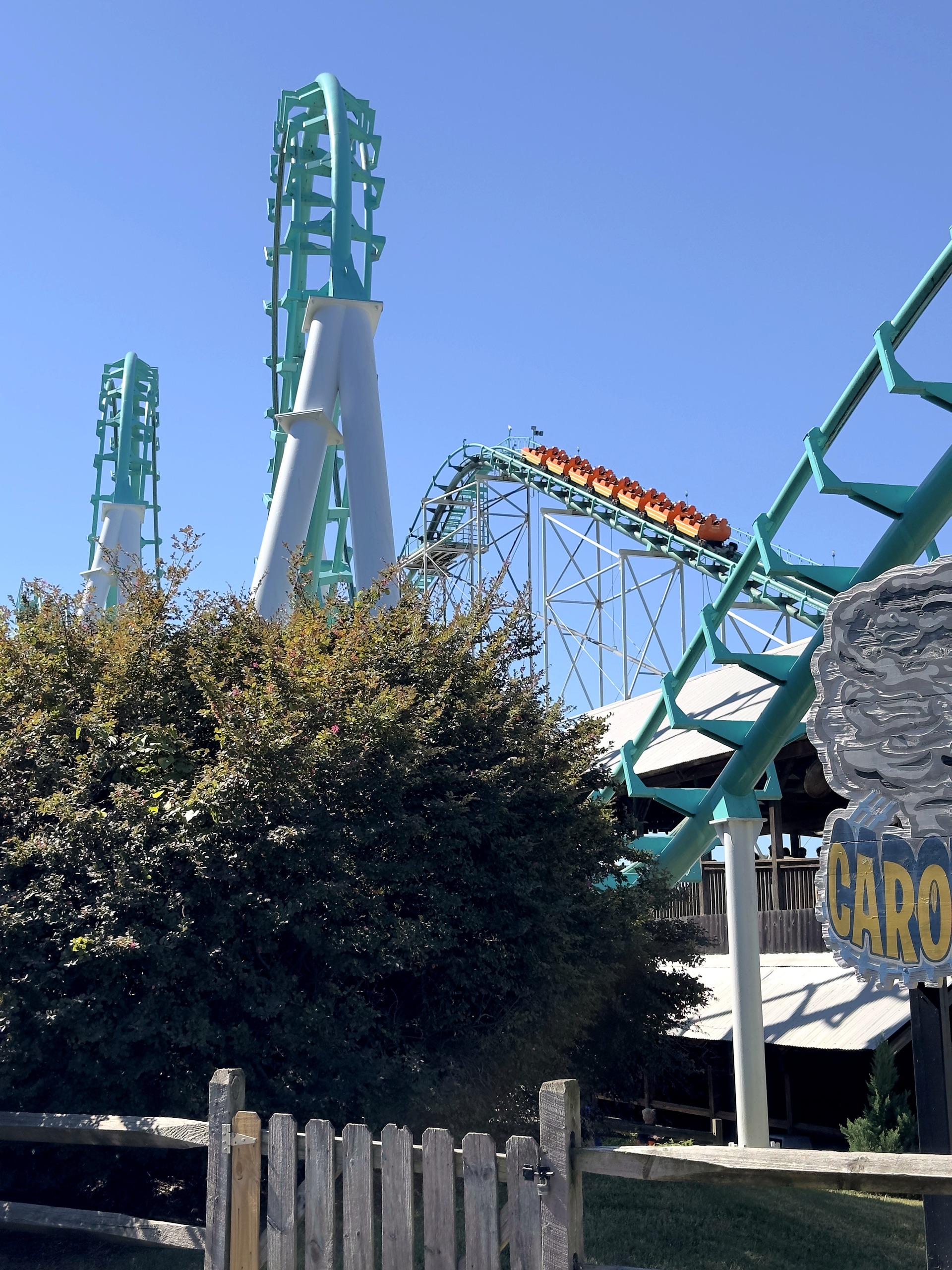 An orange Carolina Cyclone train climbing the lift hill behind the two vertical loops at Carowinds, October 2024