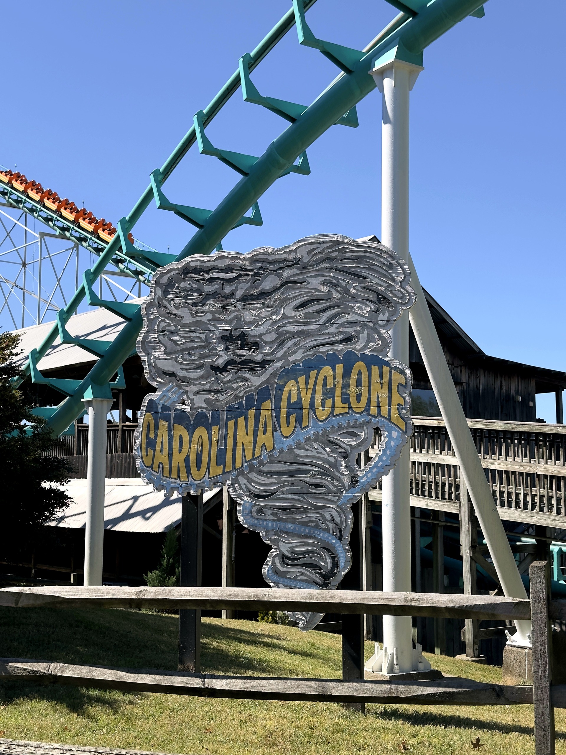 The Carolina Cyclone sign beside the teal track with an orange train on the lift behind it at Carowinds, October 2024