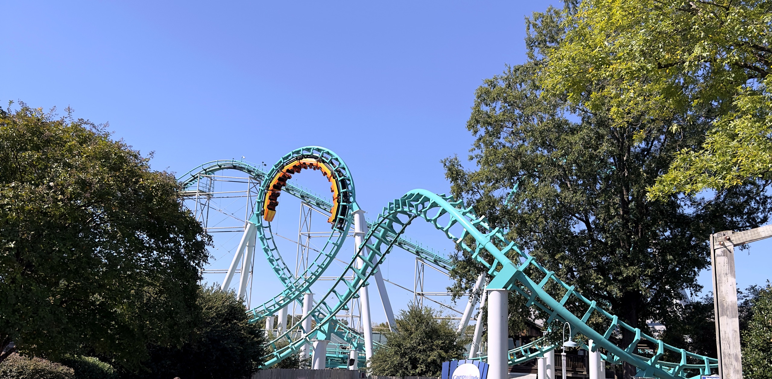 An orange Carolina Cyclone train upside down at the top of a vertical loop, framed by trees at Carowinds, October 2024