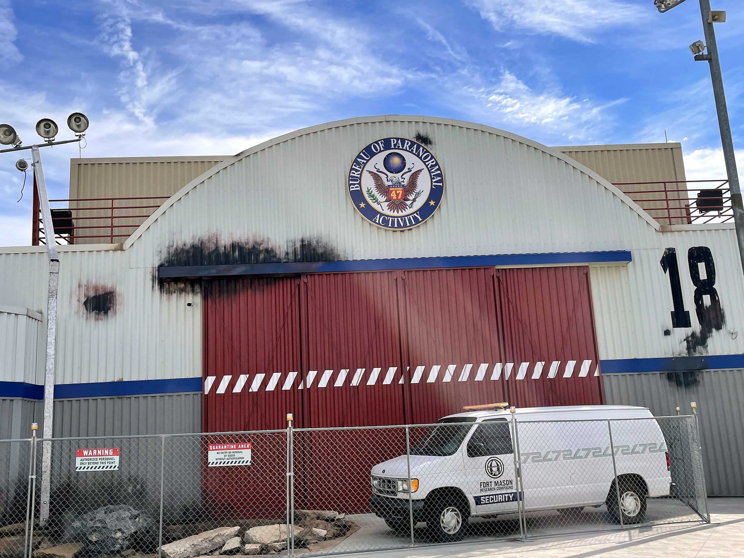 The Bureau of Paranormal Activity hangar 18 with scorched doors and a security van parked in front, Kings Island, July 2022