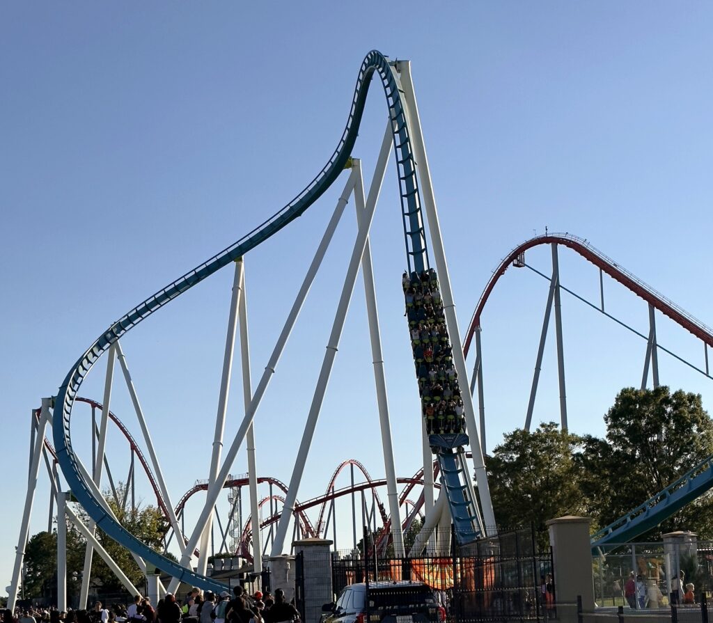 A Fury 325 train diving out of the tall banked turn above the front gate with Thunder Striker's red track behind at Carowinds, October 2024