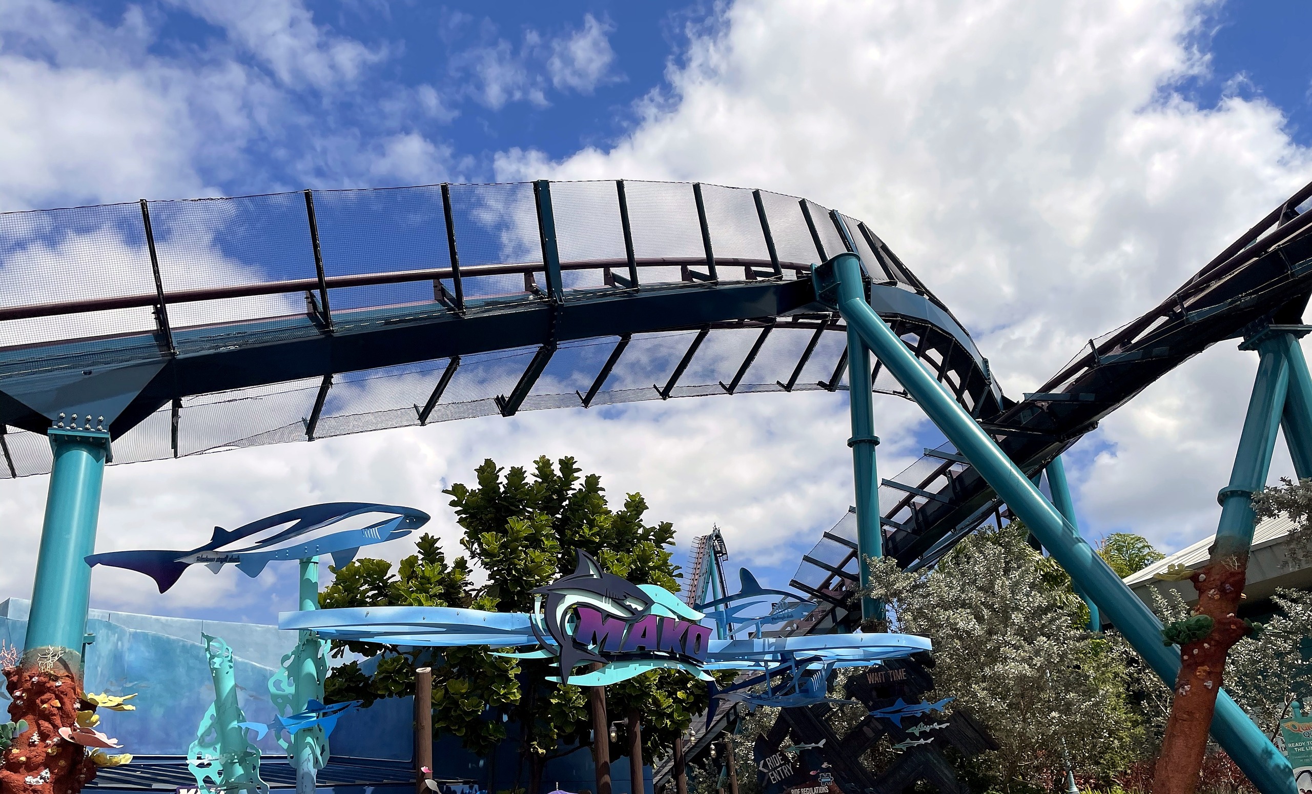 The Mako entrance sign with the shark sculptures, teal supports and track overhead at SeaWorld Orlando, March 2021