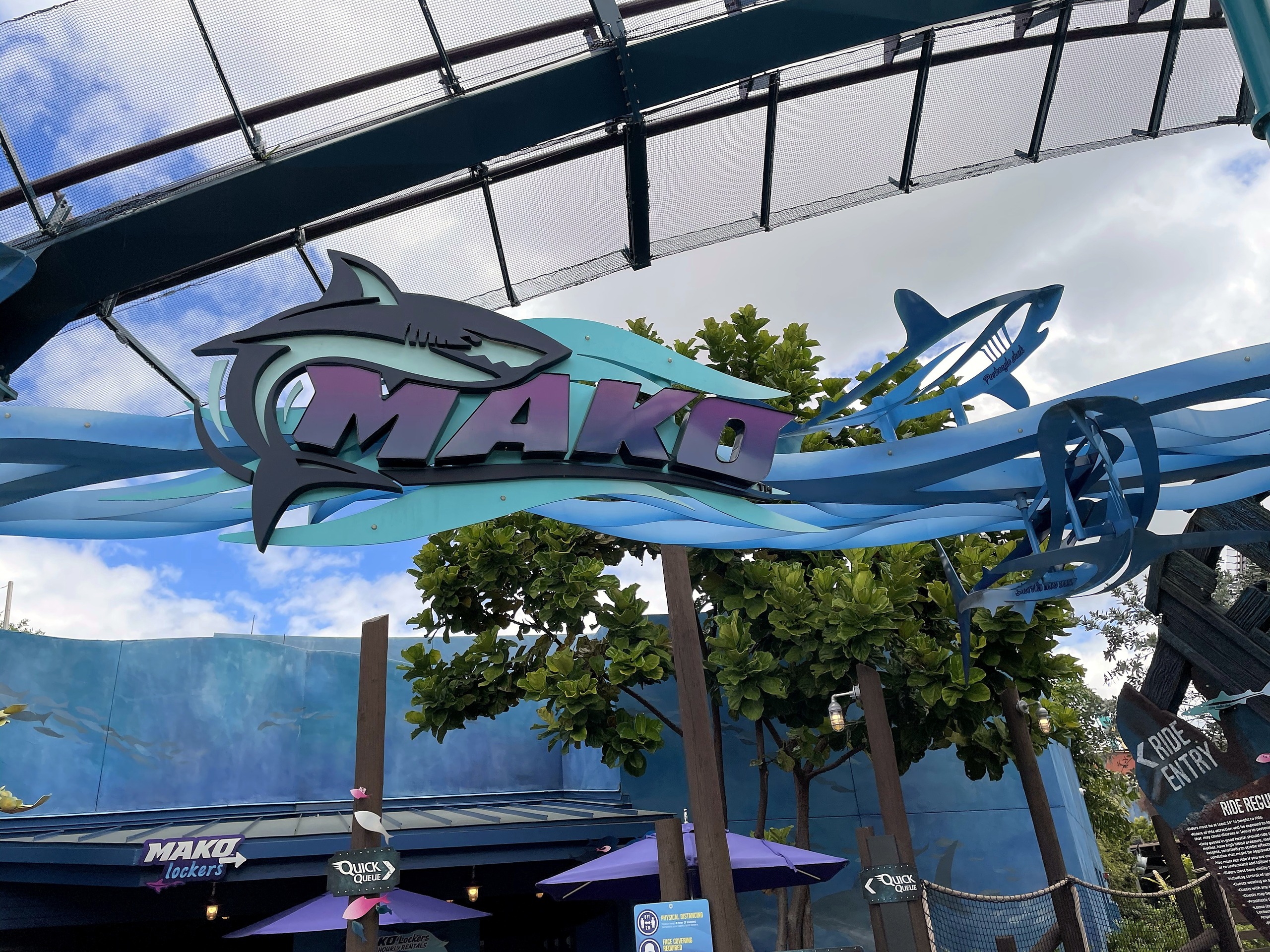 The Mako entrance sign with its shark logo under the station canopy and overhead track at SeaWorld Orlando, March 2021