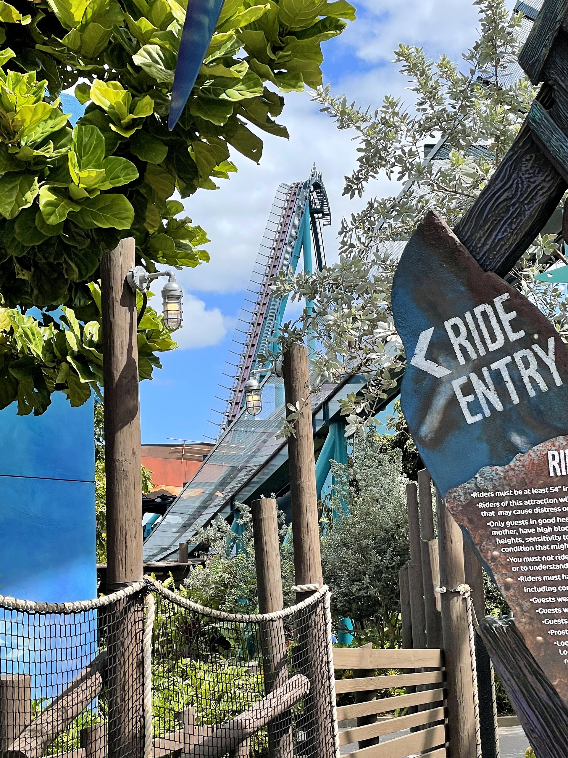 The Ride Entry sign at Mako's entrance with the lift hill through the trees at SeaWorld Orlando, March 2021