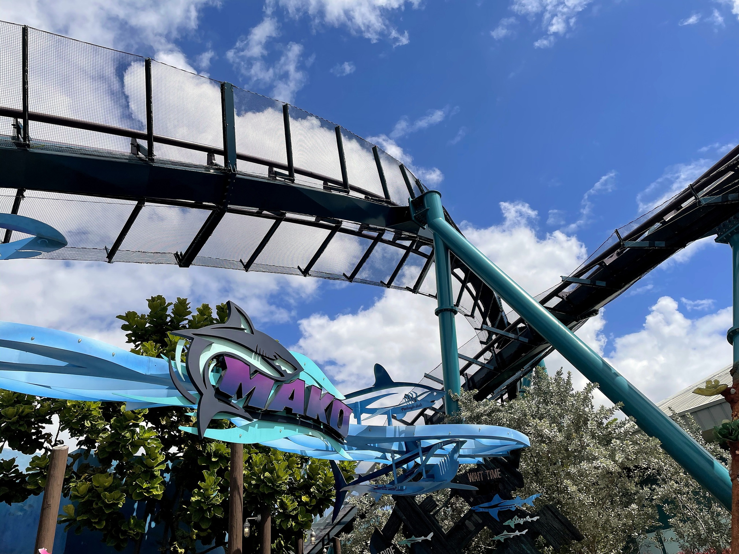 The Mako sign beneath a teal support with the track curving overhead against a blue sky at SeaWorld Orlando, March 2021